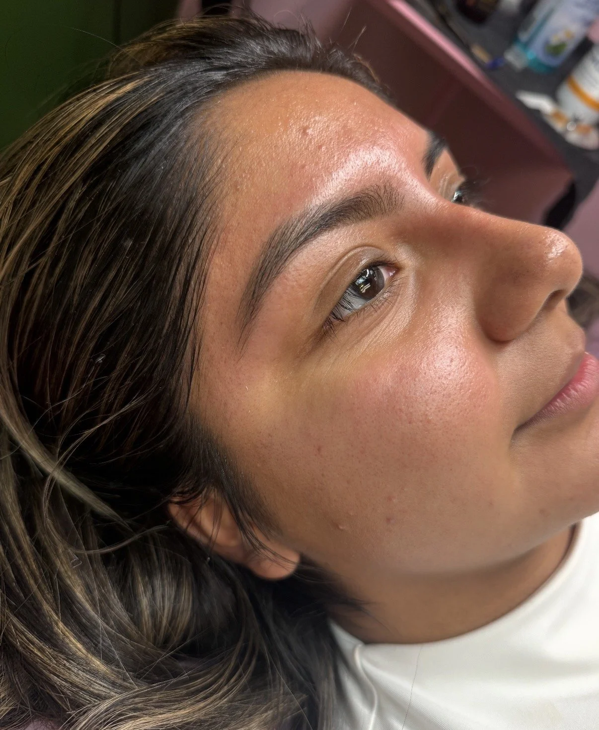 Close-up of a woman with well-groomed eyebrows, smooth skin, and brown hair lying down in a salon or spa setting.