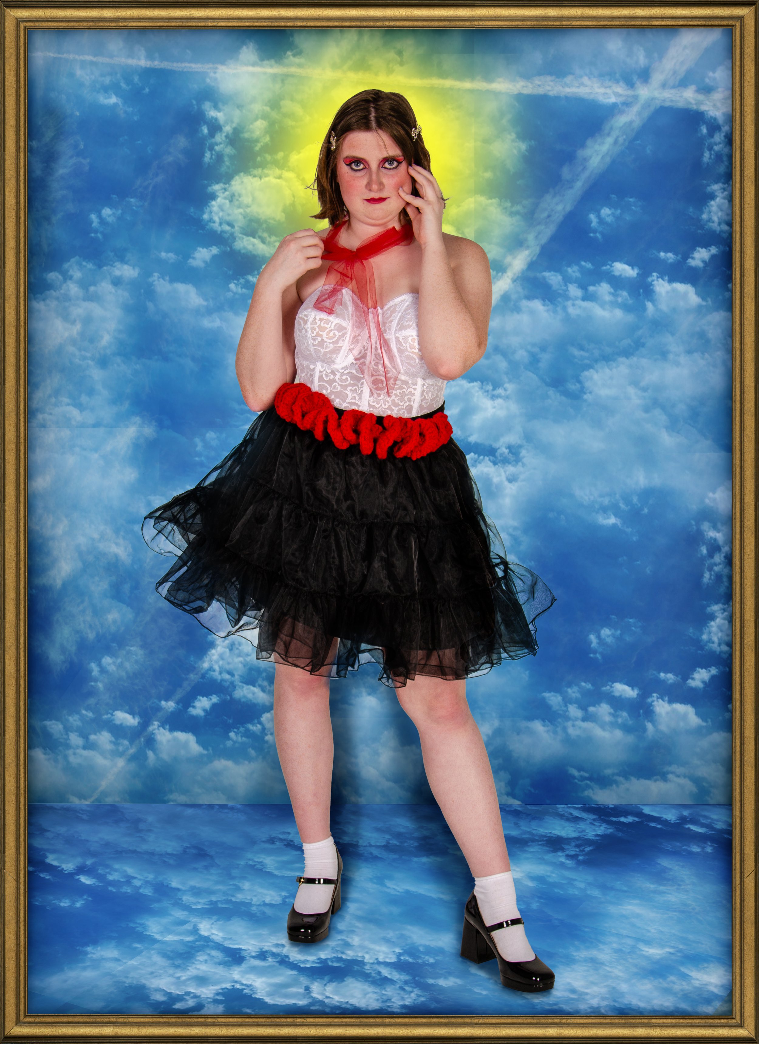 A person with short brown hair, makeup, and artistic eye design, dressed in a white lace top, red scarf, black tulle skirt with red ruffle details, white socks, black high heels, standing against a cloud and sky background with a glowing halo effect