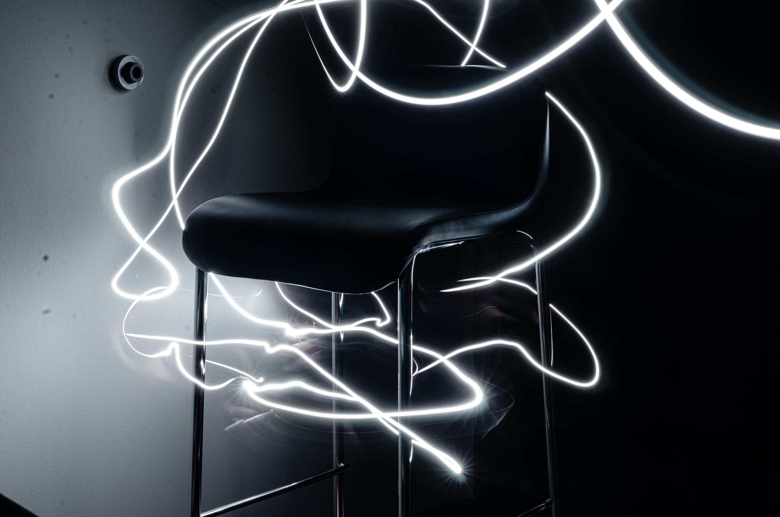 A black chair with chrome legs surrounded by glowing white light trails in a dark room.