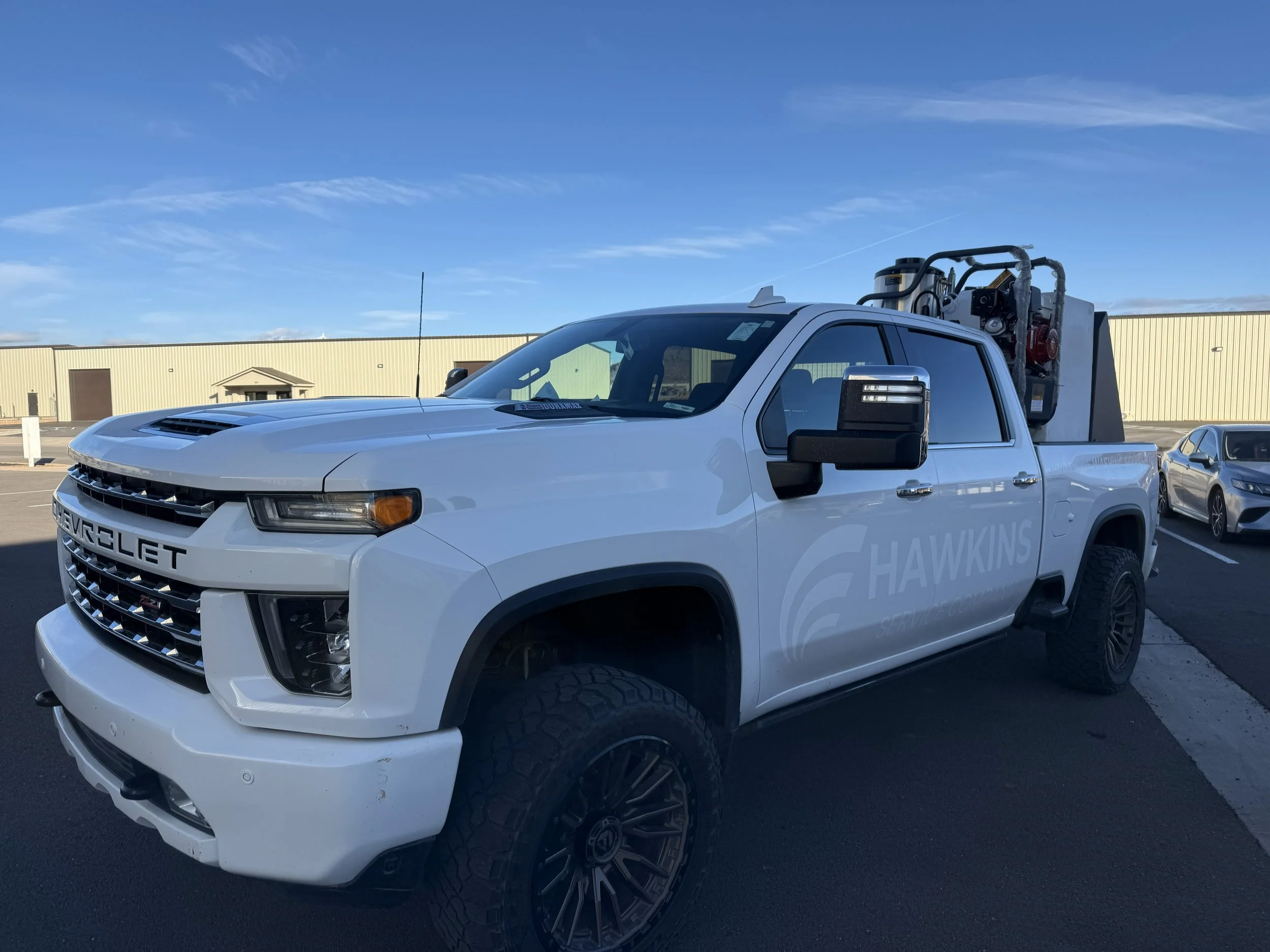 White Chevrolet pickup truck with service equipment on the back, parked in a lot under a blue sky.
