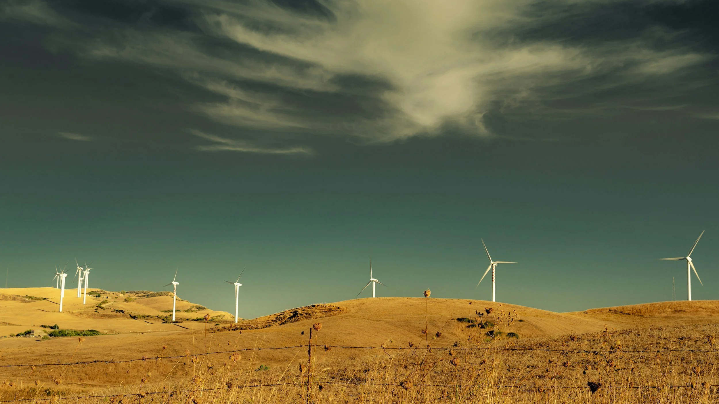 Rolling hills under a partly cloudy sky with several white wind turbines scattered across the landscape.