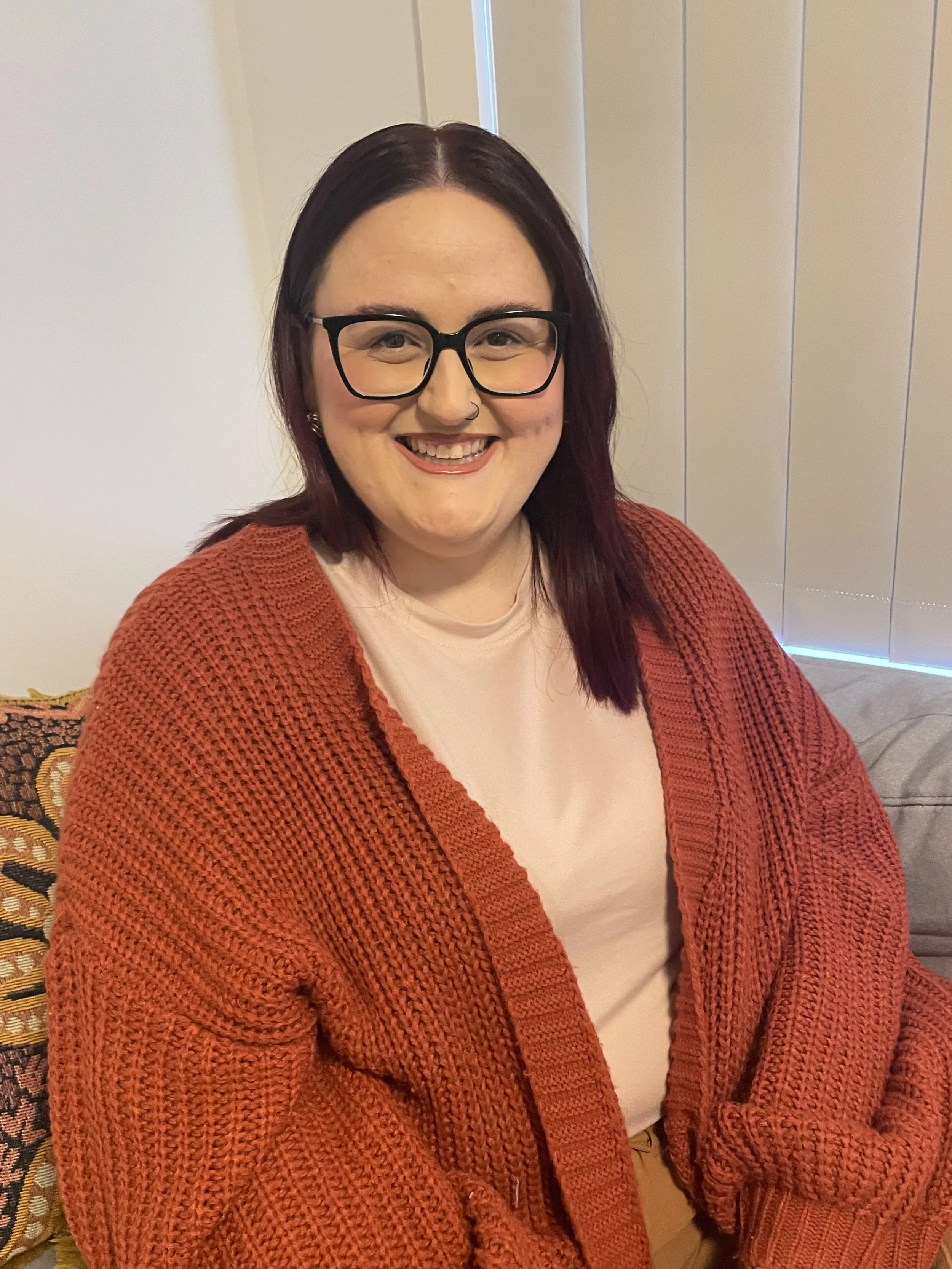 Person with glasses, pink hair, wearing brown and white striped sweater, outdoors.