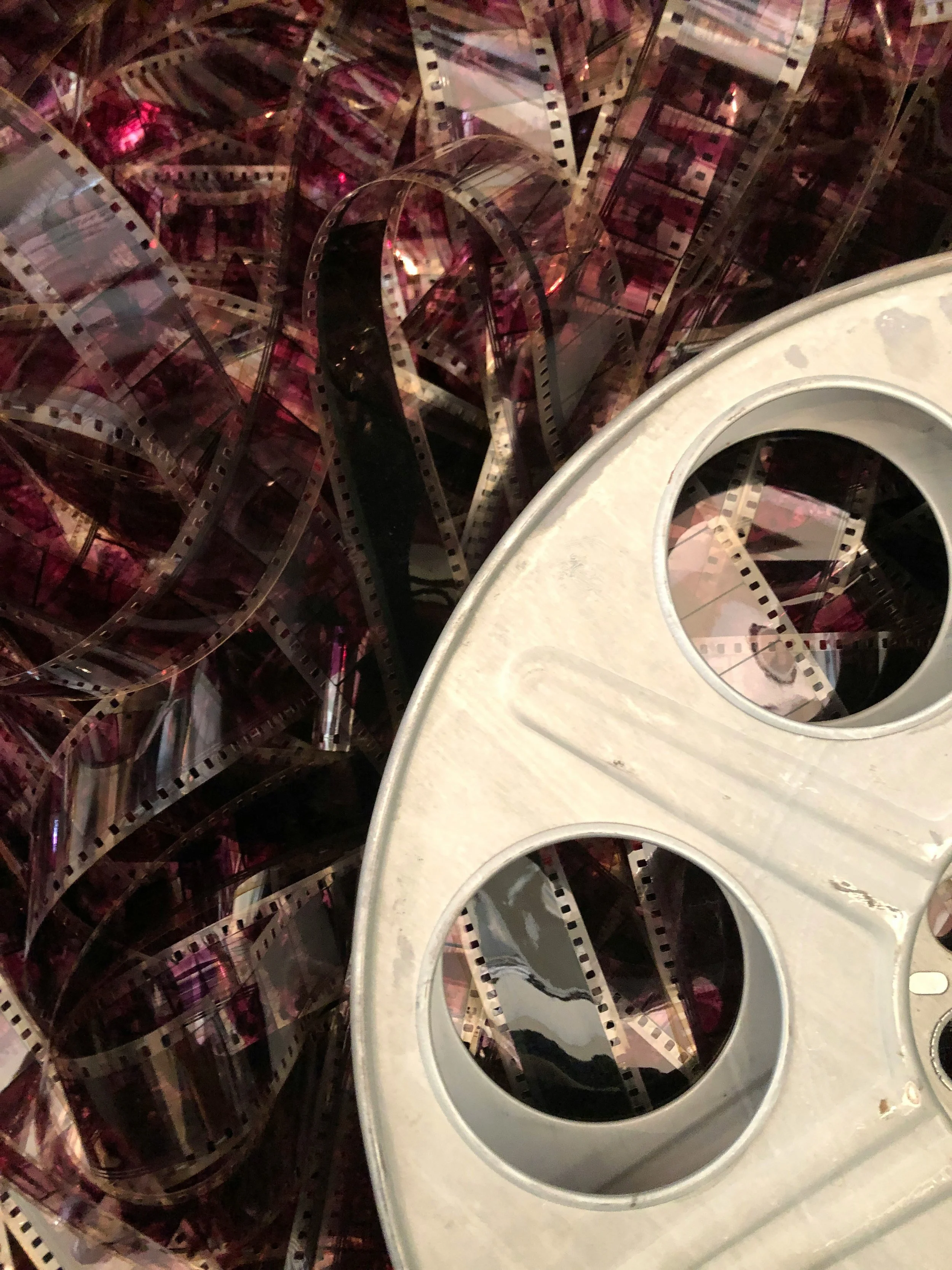 A collection of film strips in a pile, partially surrounded by a white film reel with empty circular slots.