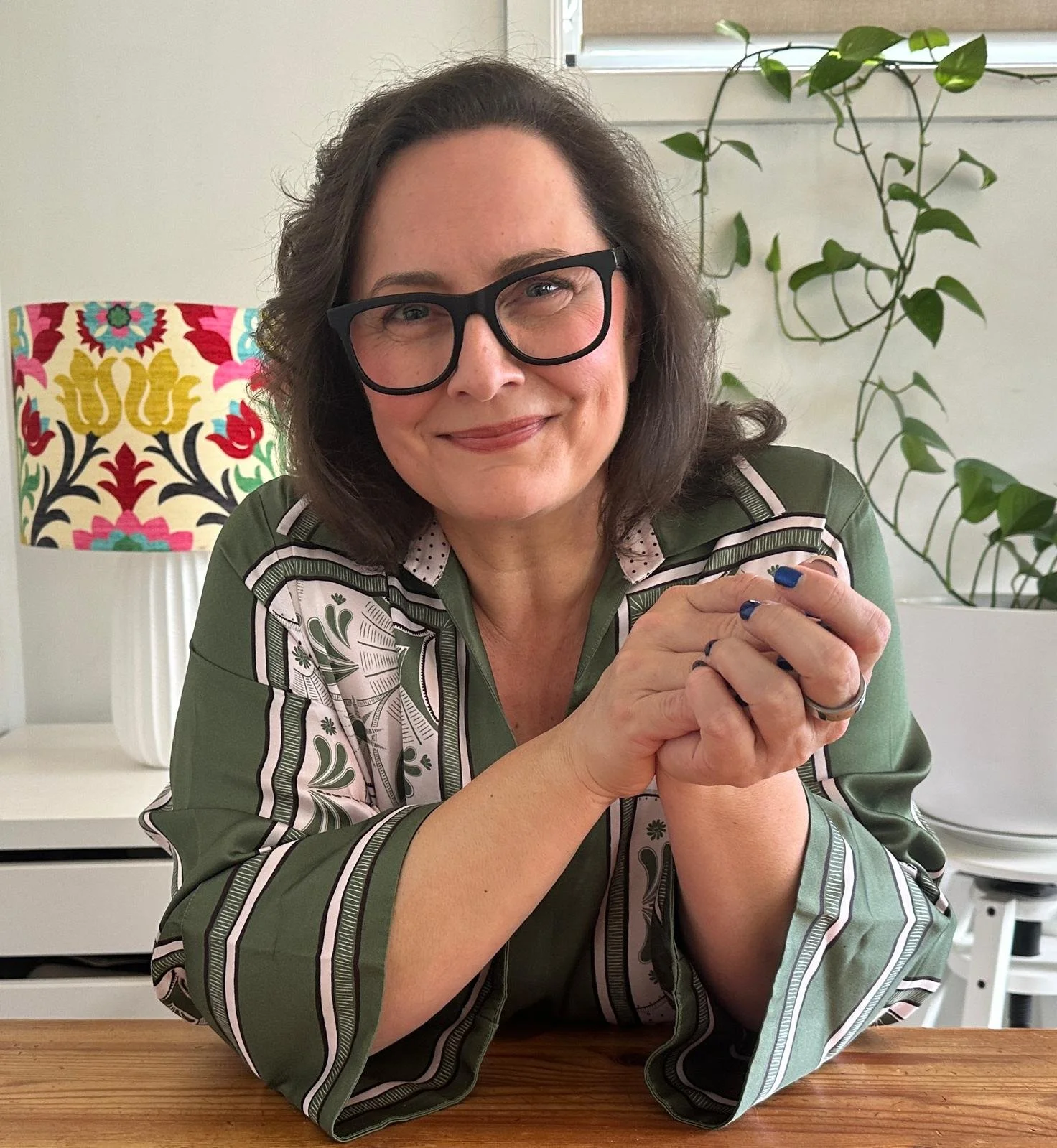 Person with glasses and white shirt smiling in front of a hedge.