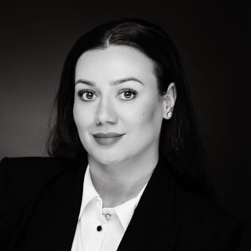 Black and white portrait of a woman with dark hair, wearing a suit jacket and white shirt, looking directly at the camera.