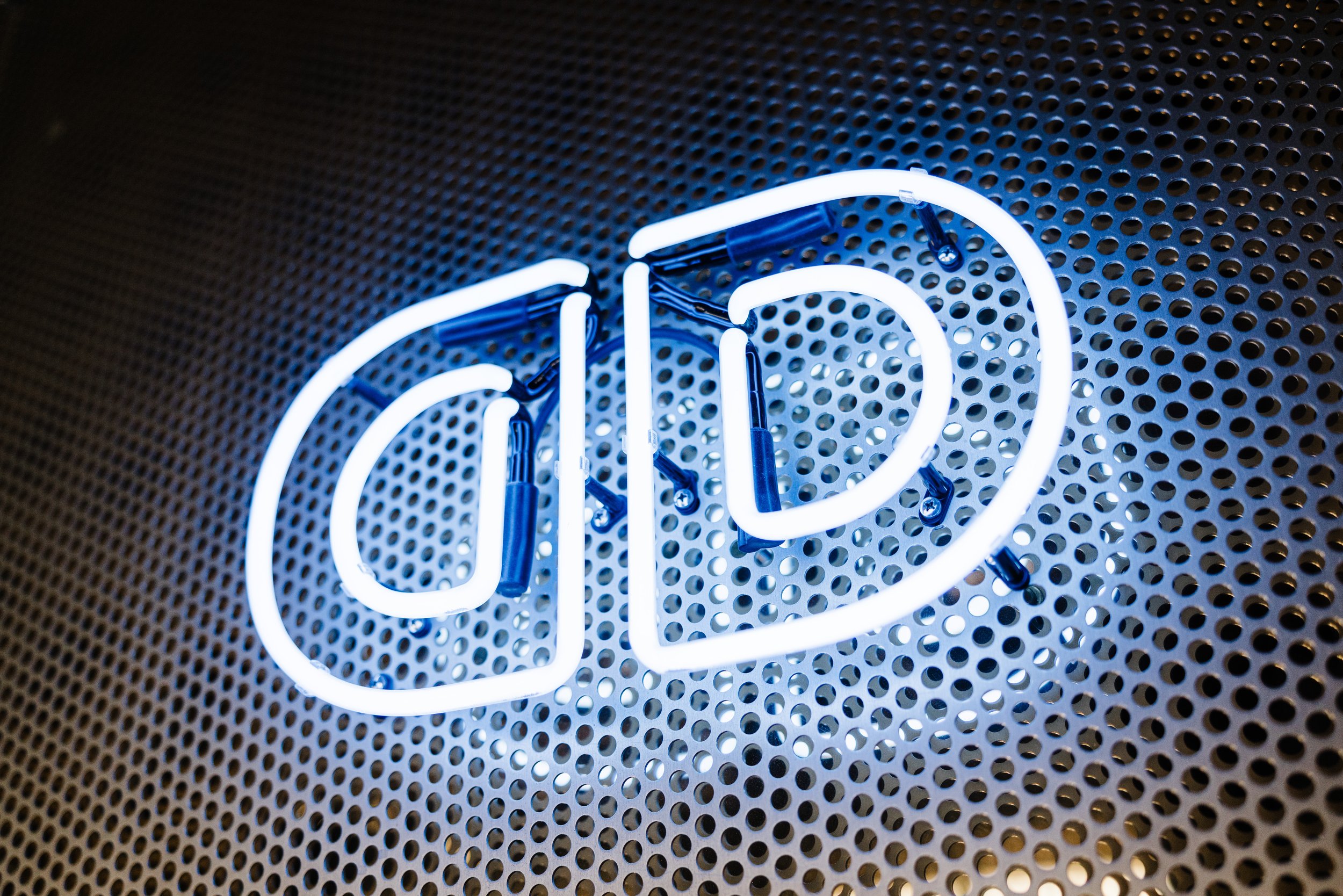 Blue and white neon sign reading 'DD' against a perforated metal background.