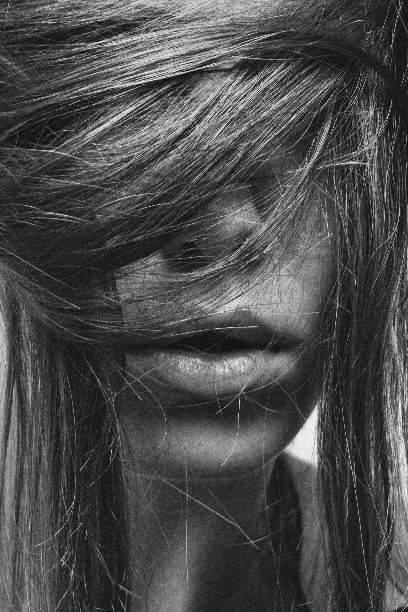 Black and white close-up photo of a woman's face with her hair covering her eyes, lips slightly parted.