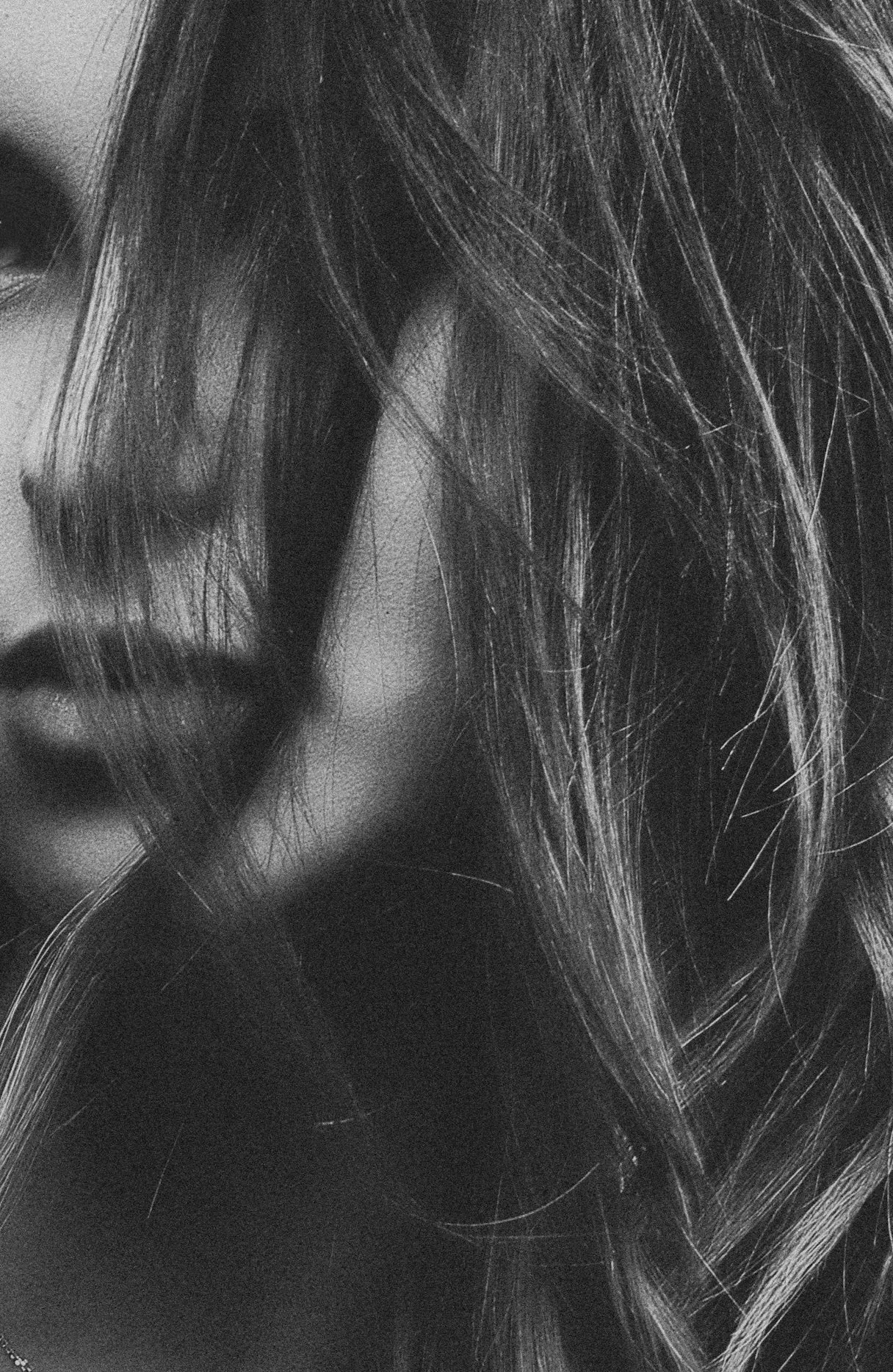 Close-up black and white photo of a woman's face with long, tousled hair covering part of her face, focusing on her lips and cheek.