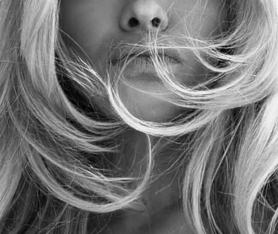 Close-up of a woman's face, partially obscured by flowing blonde hair in black and white.