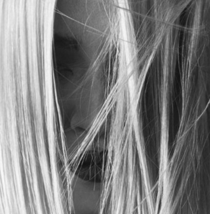 Close-up of a woman's face partially covered by her hair in black and white.