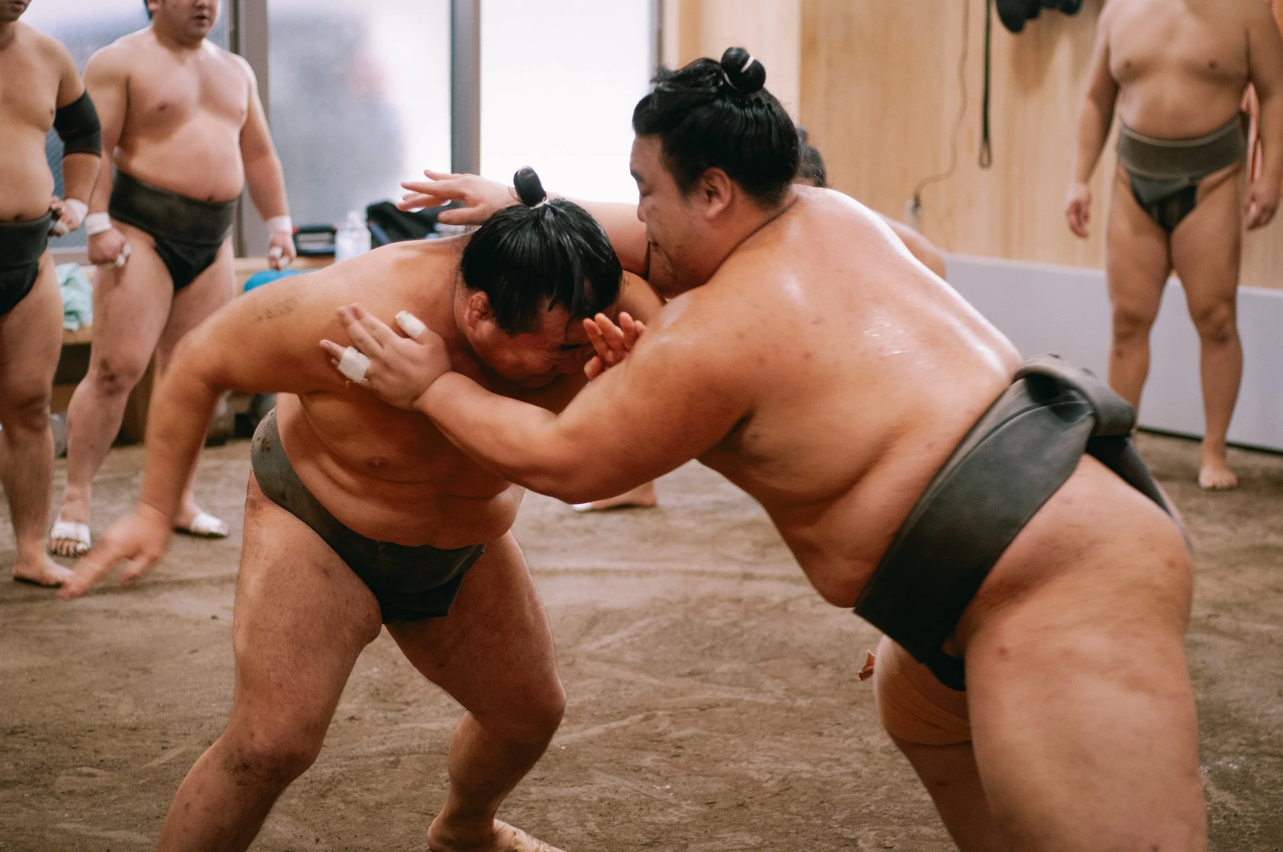 Two sumo wrestlers sparring in a ring, surrounded by other sumo wrestlers watching.
