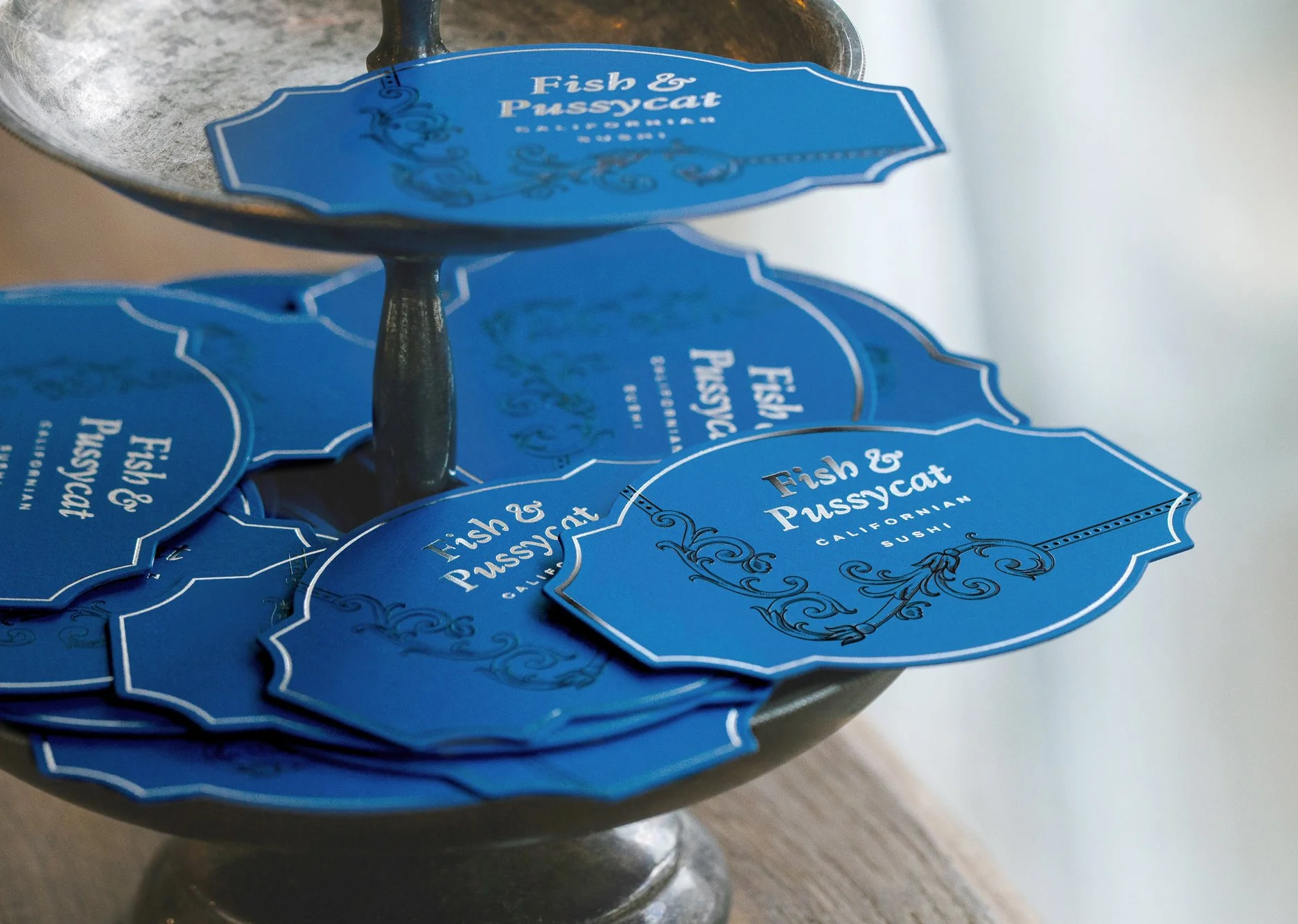 Blue business cards for Fish & Pussycat, a Californian sushi restaurant, are displayed on a metal stand.