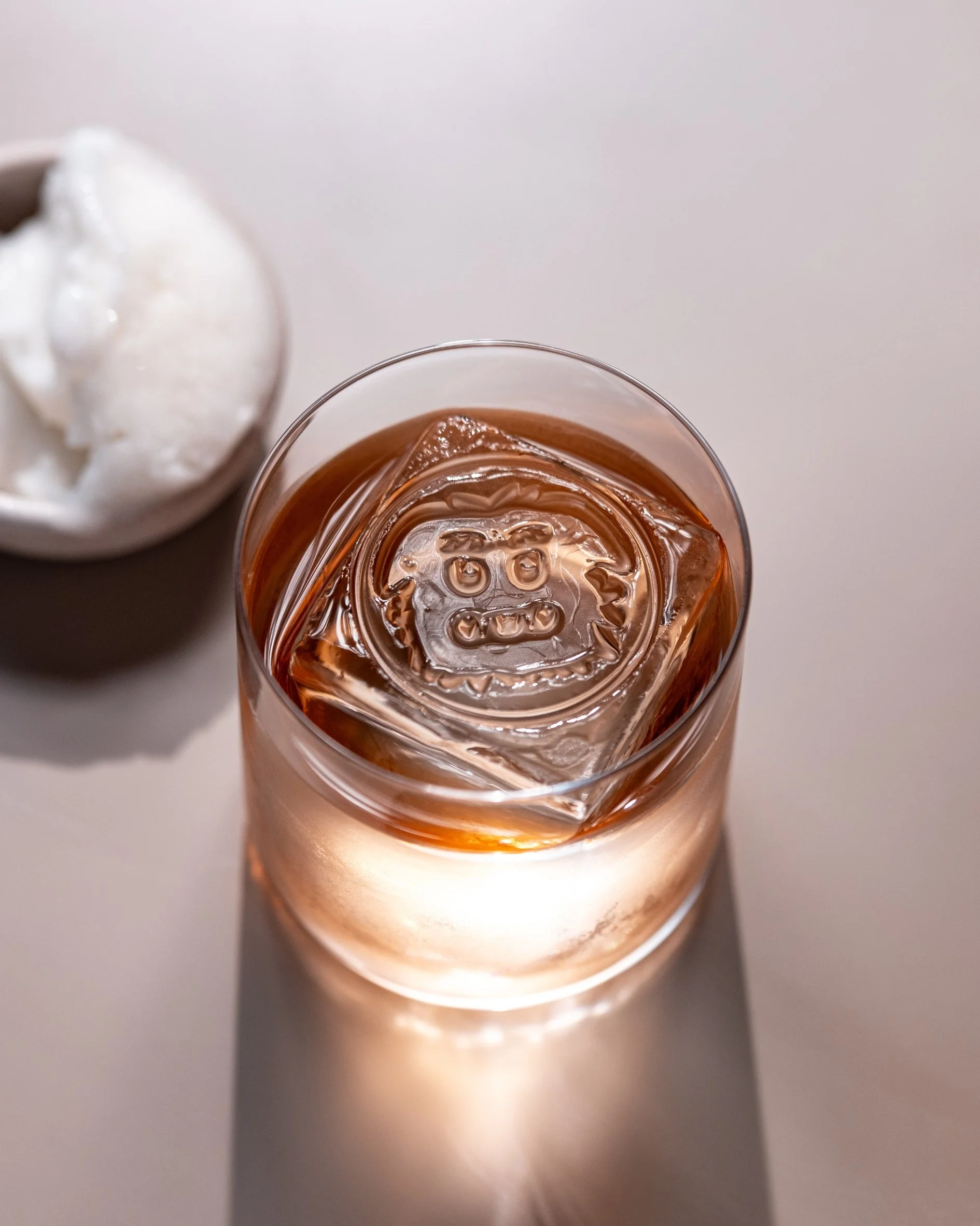 Close-up of a glass of iced tea with ice cubes and a bowl of whipped cream in the background.