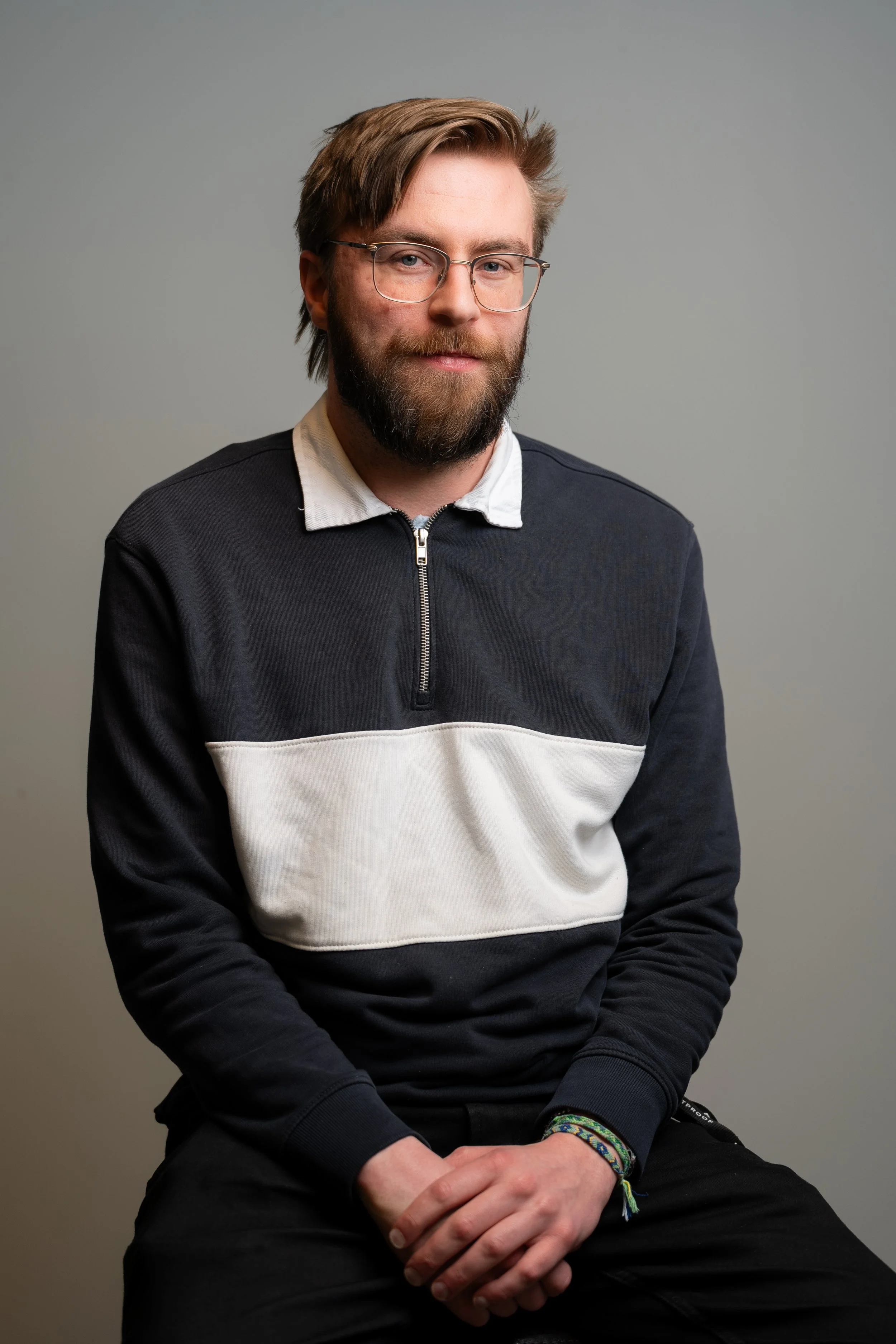 A man with dark hair, glasses, and a beard wearing a white dress shirt against a blurred background.