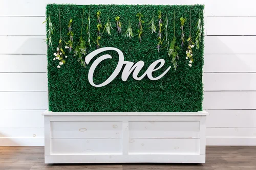 'One' sign with florals on the greenery wall
