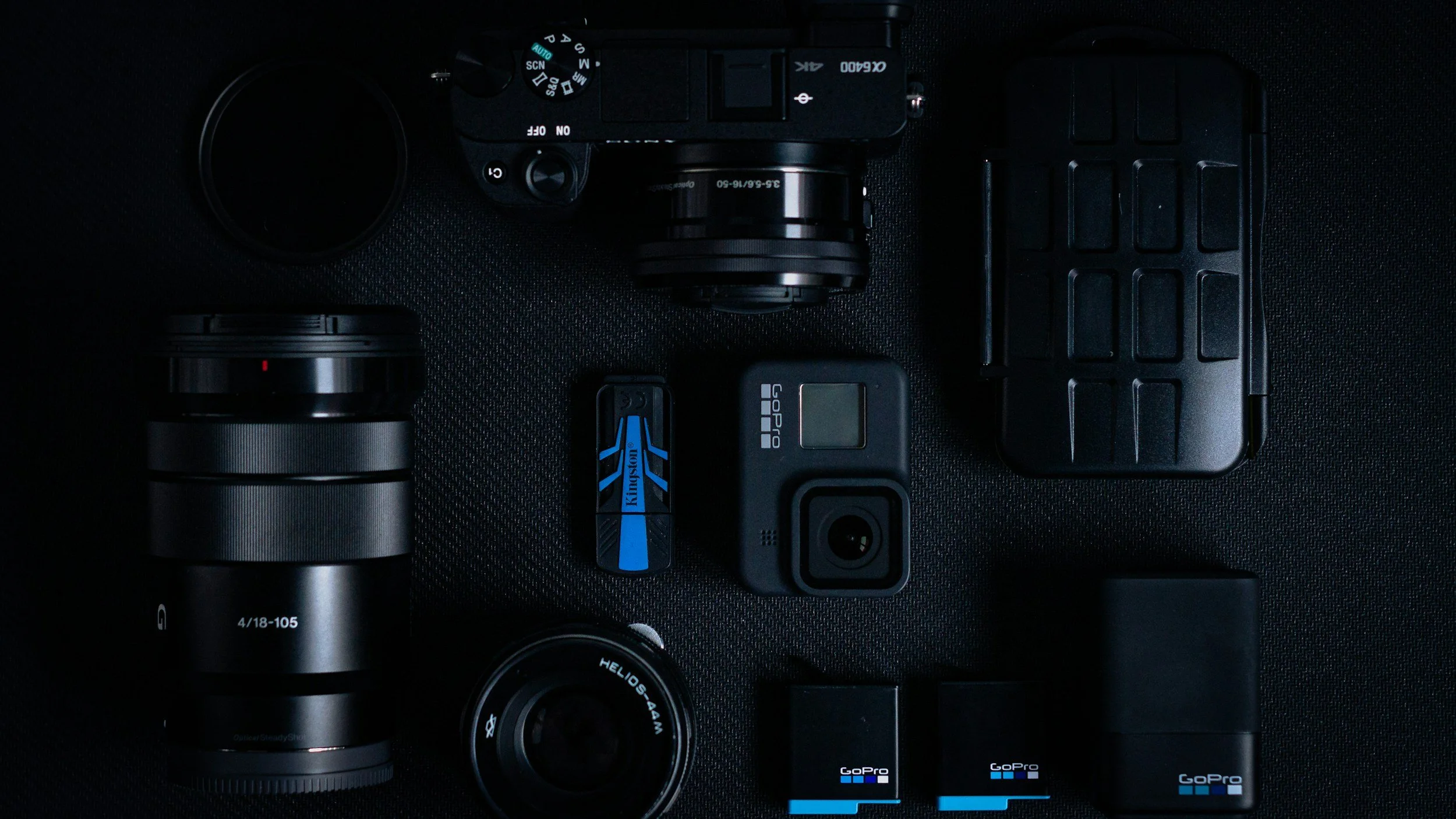 A camera a go pro with batteries and lenses on a table