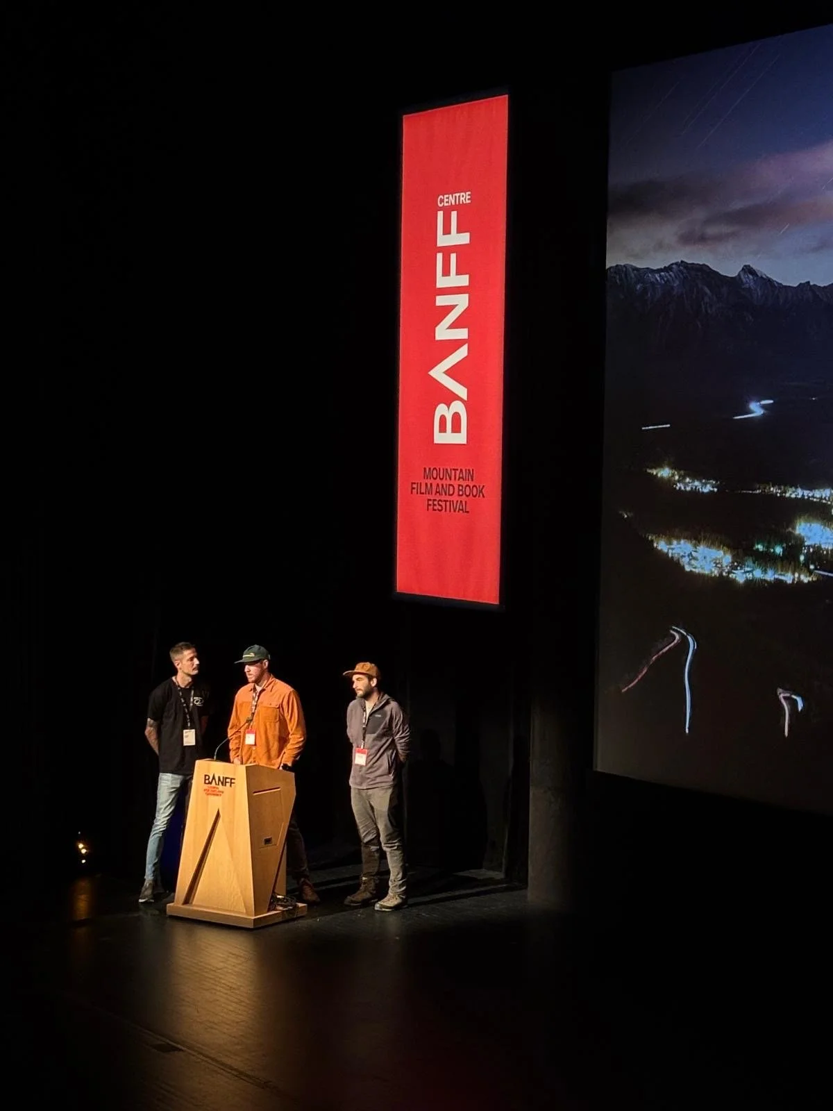 Three people standing under the BANFF film festival banner on stage