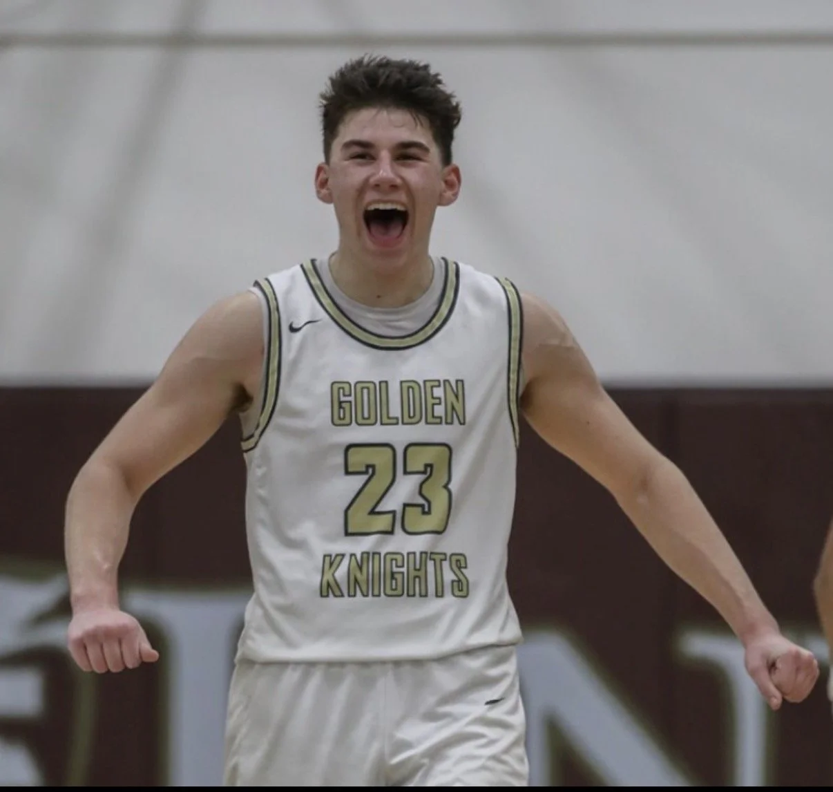 A young male basketball player wearing a white jersey with the words "GOLDEN KNIGHTS" and the number 23, celebrating with a triumphant expression on his face.