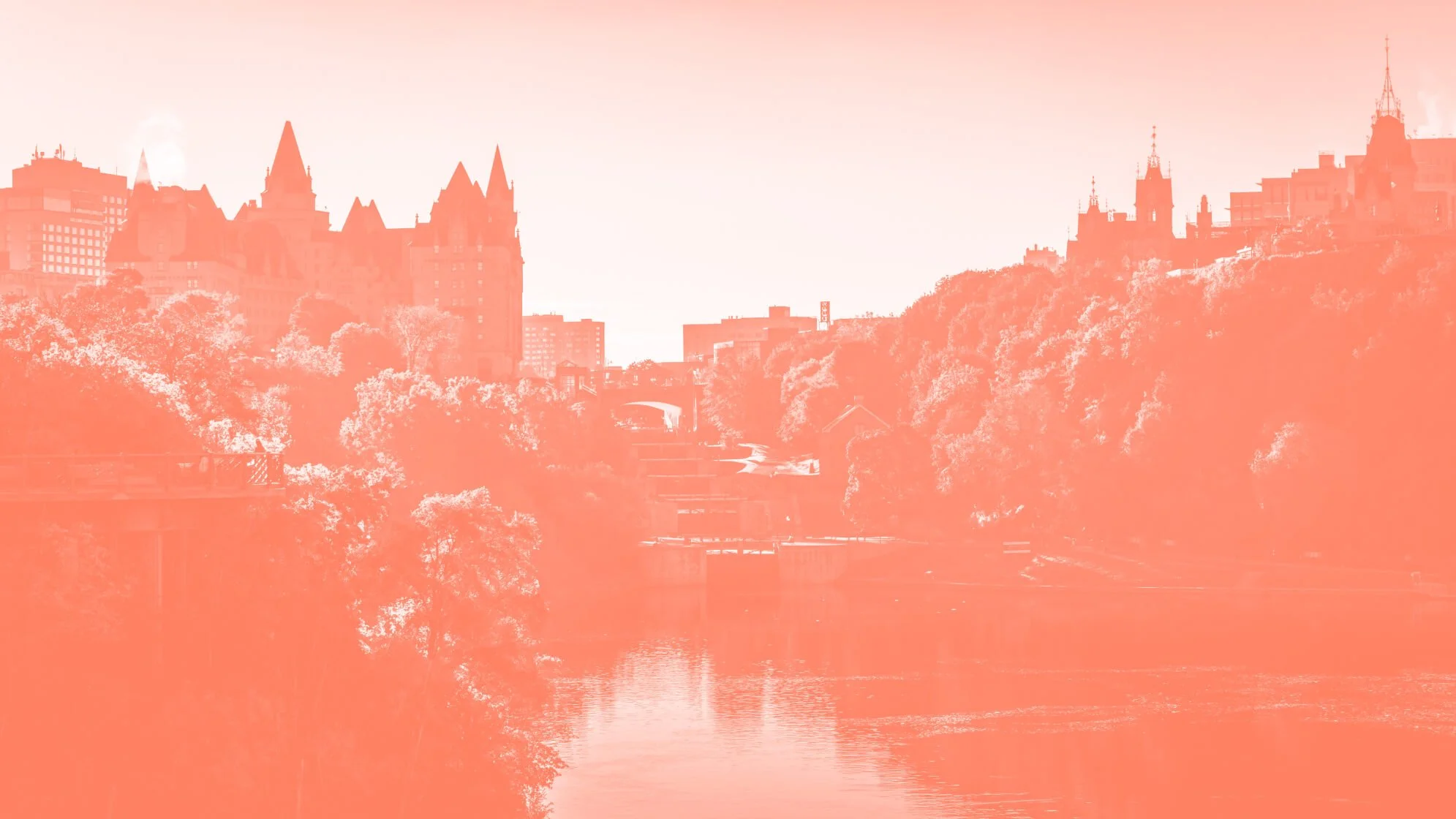 A city skyline with historic castle-like buildings on a hill, overlooking a river with trees on both banks in the foreground, bathed in a pinkish-orange hue.