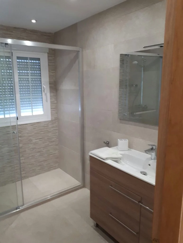 Bathroom with a walk-in shower, a window with blinds, a mirror above a wooden vanity with a sink, and towels on the vanity