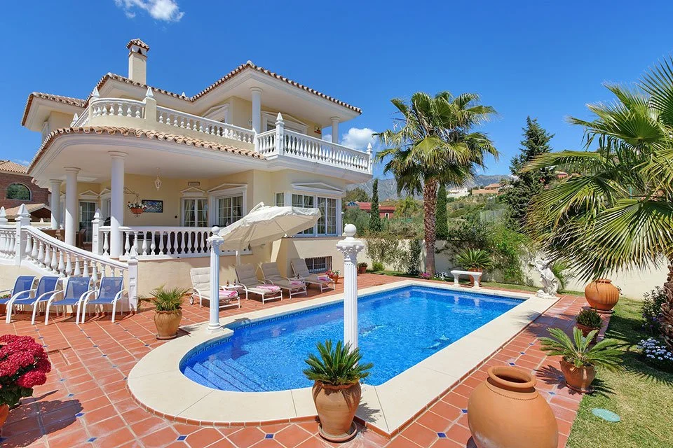 Luxury house with a swimming pool, palm trees, and patio furniture.