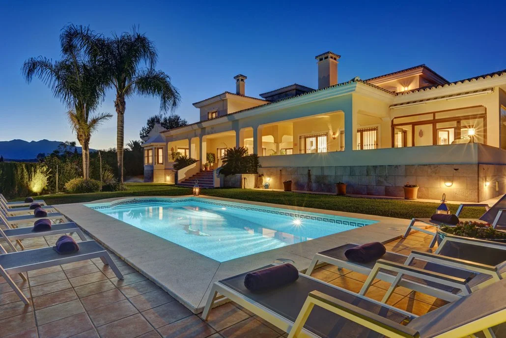 Luxury house with a pool and lounge chairs in the backyard during twilight.