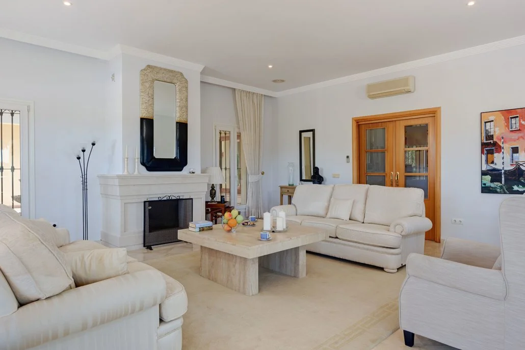 Living room with white sofas, a stone fireplace, a wooden coffee table, and a flat-screen TV on the wall.