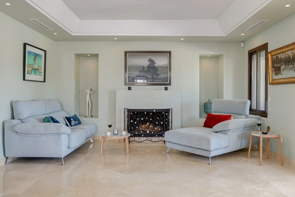 Living room with white sofas, a fireplace, artwork, and a window with wooden trim.