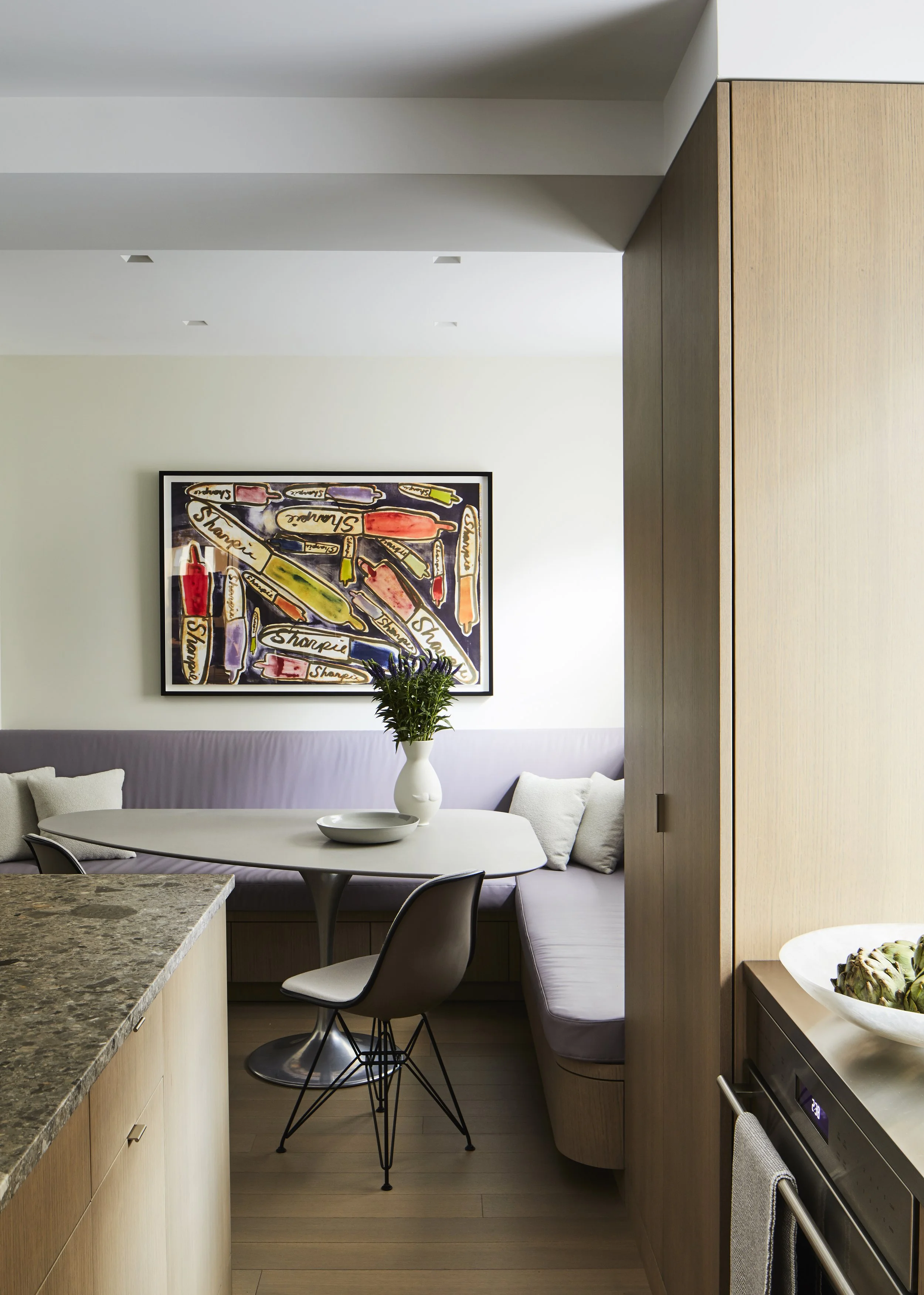 Modern dining area with a table, chairs, a vase with greenery, and a colorful abstract wall art.