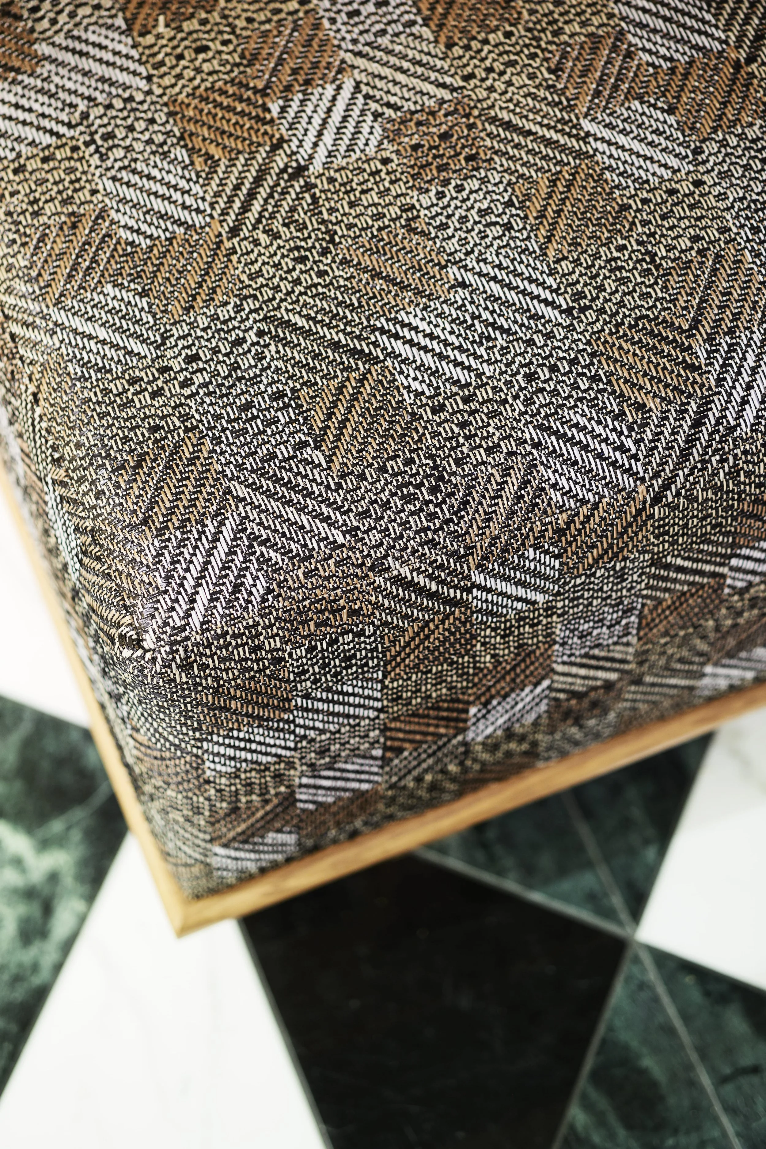 Close-up of textured fabric with geometric patterns in brown, black, and white on a piece of furniture, with black and white tiled flooring below.
