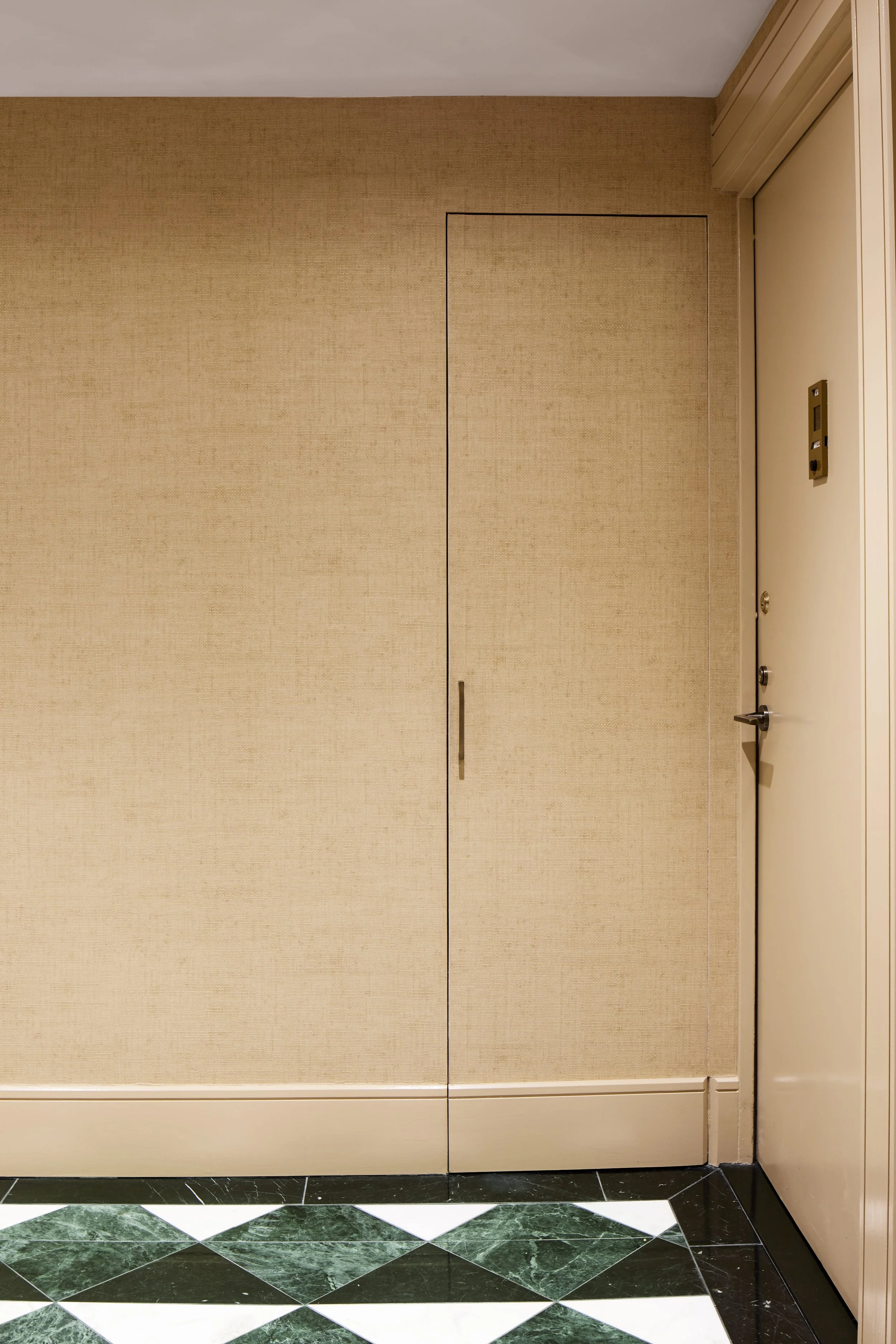 A beige wall with a door and an elevator door to the right, along with a patterned floor.