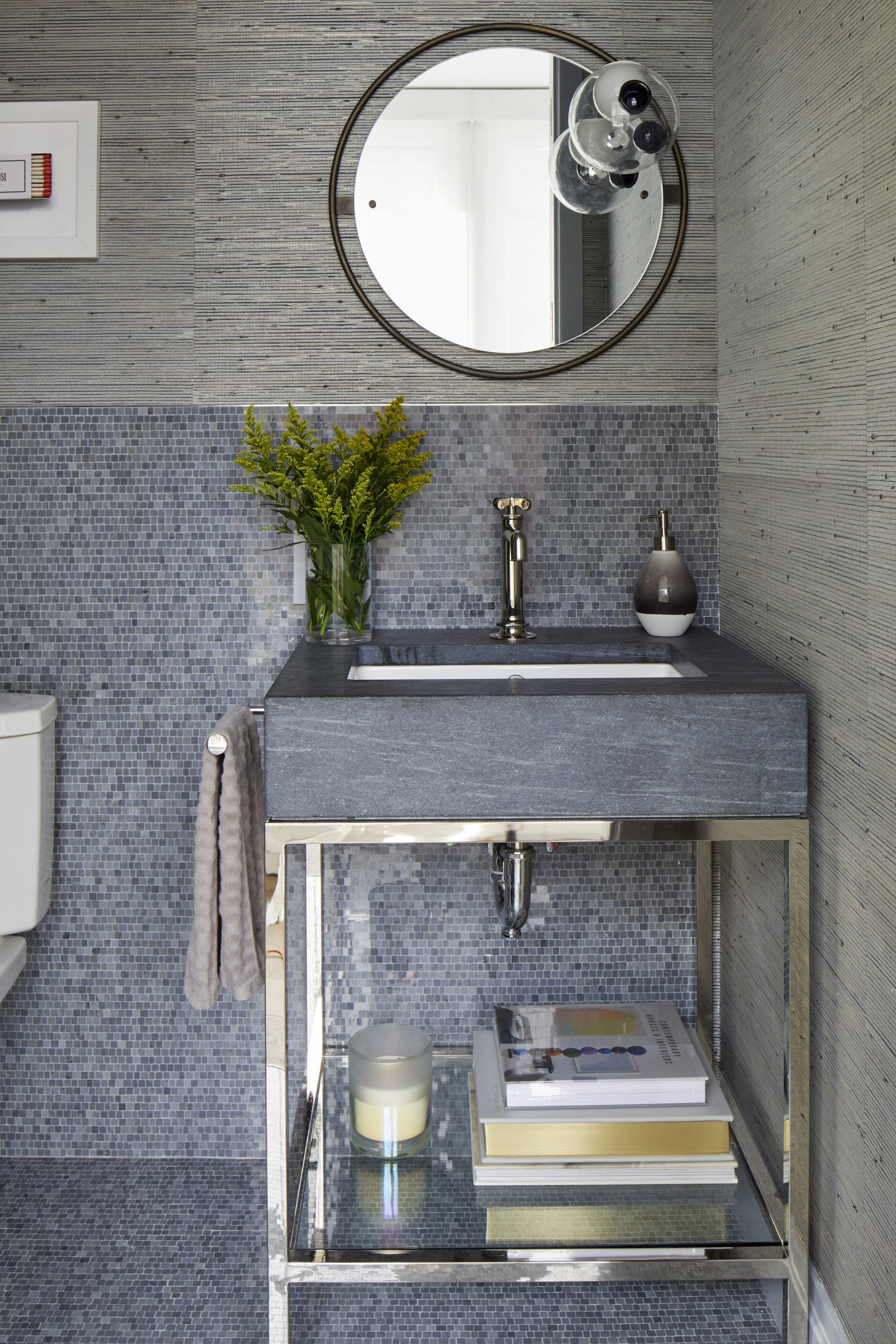 A modern bathroom vanity with a gray sink, chrome faucet, a vase with green plants, and a soap dispenser, with a round mirror and decorative glass orbs above.