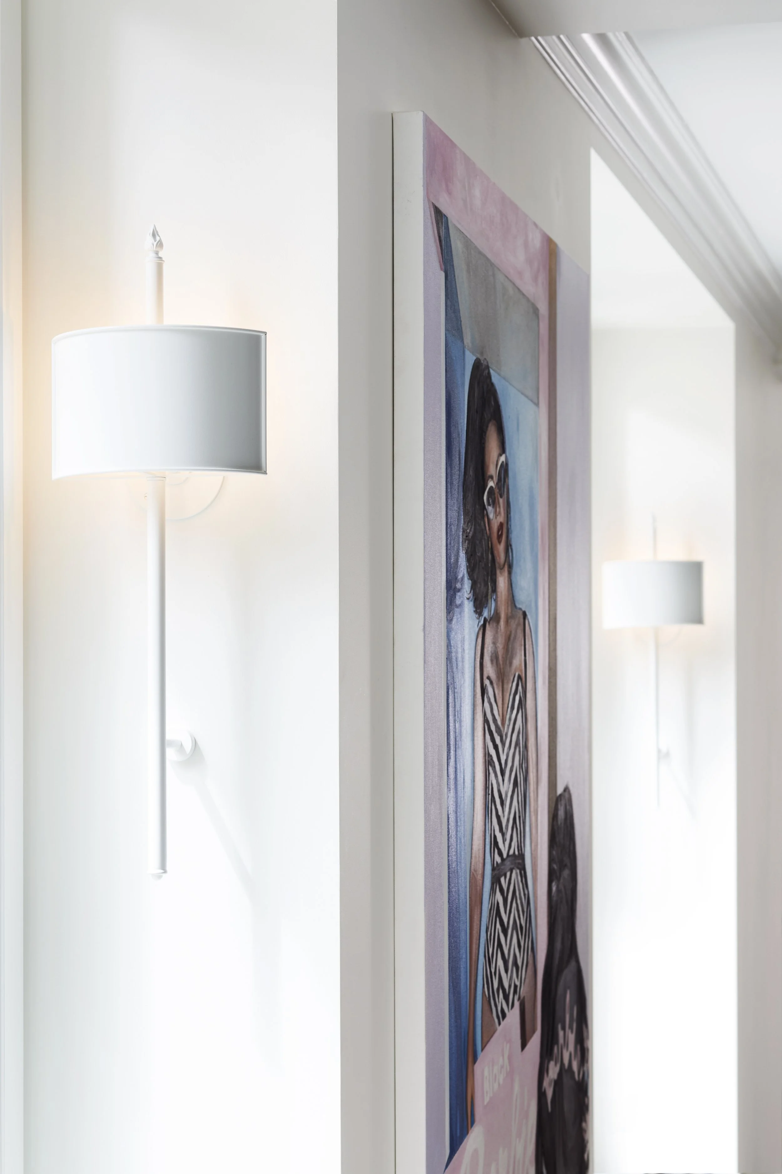 Partial view of a portrait painting of a woman with dark, wavy hair, wearing glasses and a chevron-patterned dress, hanging on a white wall with modern wall-mounted lamps illuminating the space.