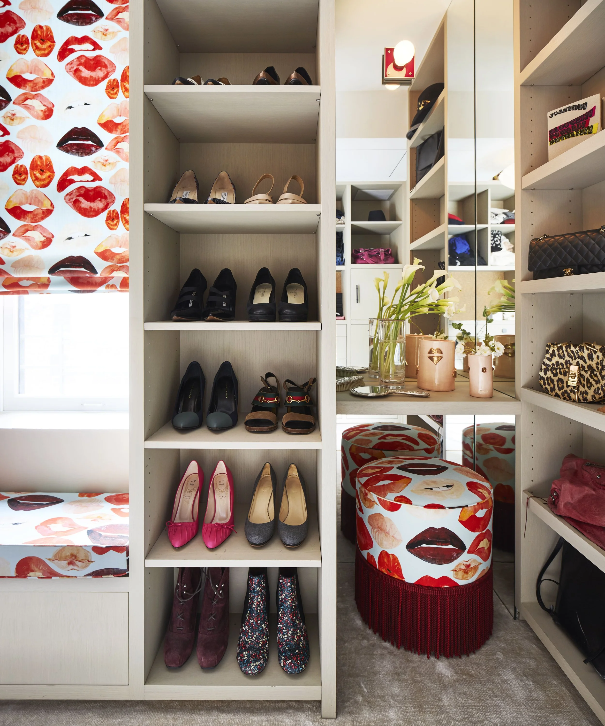 A walk-in closet with shelves of high heels, a vanity with flowers, and covered with decorative chairs featuring lips and lips pattern.