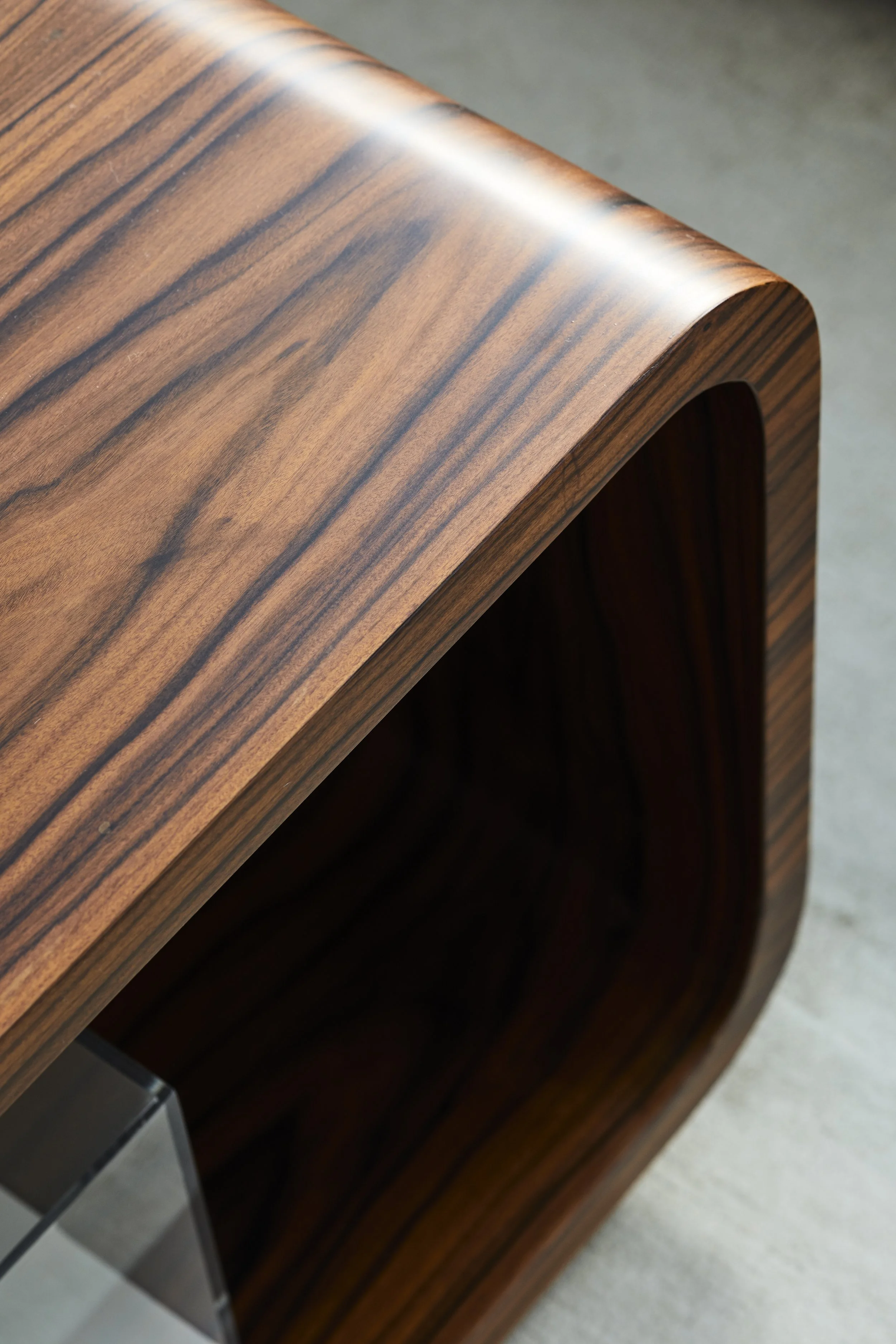 Close-up of a wooden piece with a curved edge, showcasing a polished finish and natural wood grain patterns.