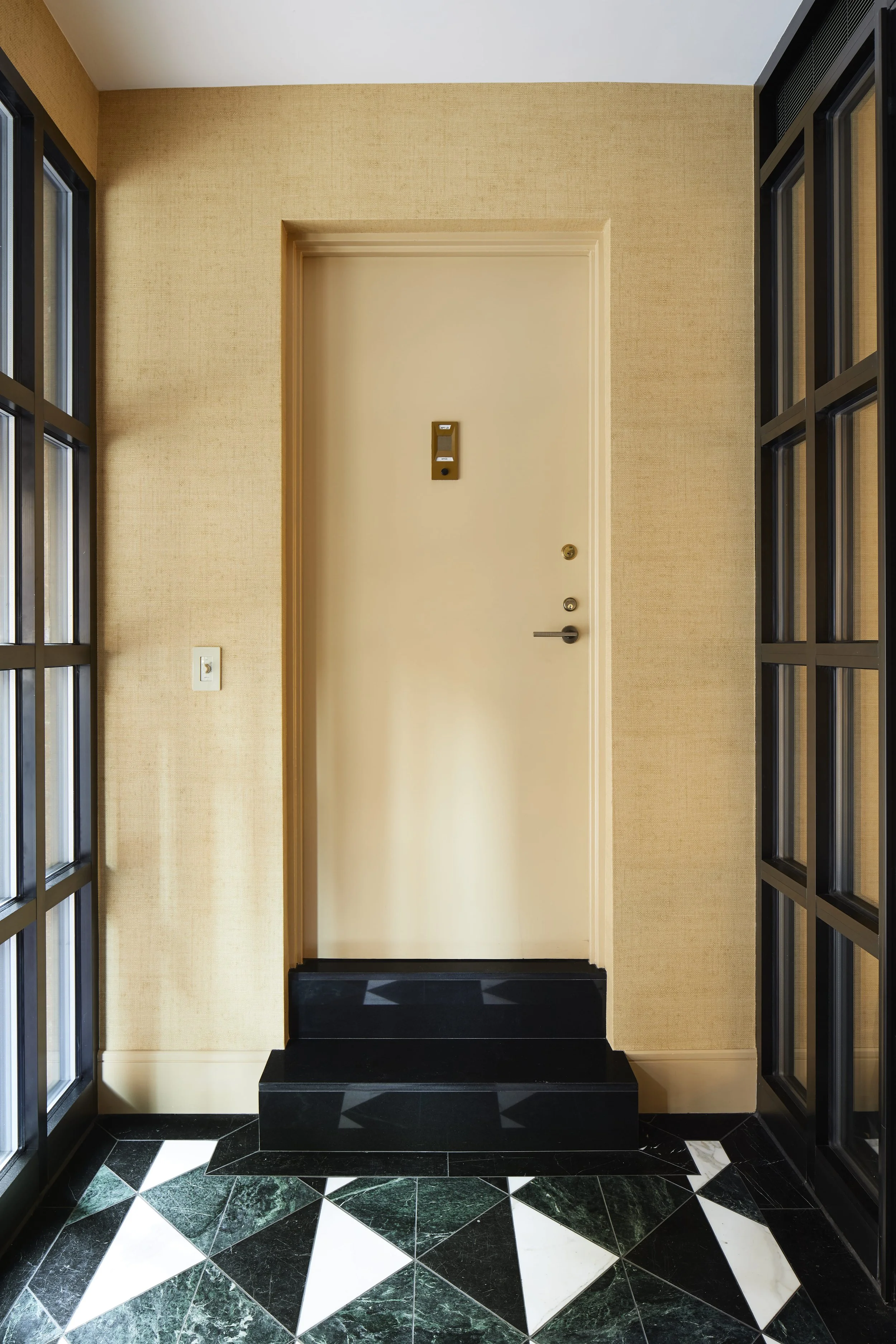 Interior view of an apartment entrance with a closed white door, black steps, beige textured walls, and glass-paneled black doors on both sides.