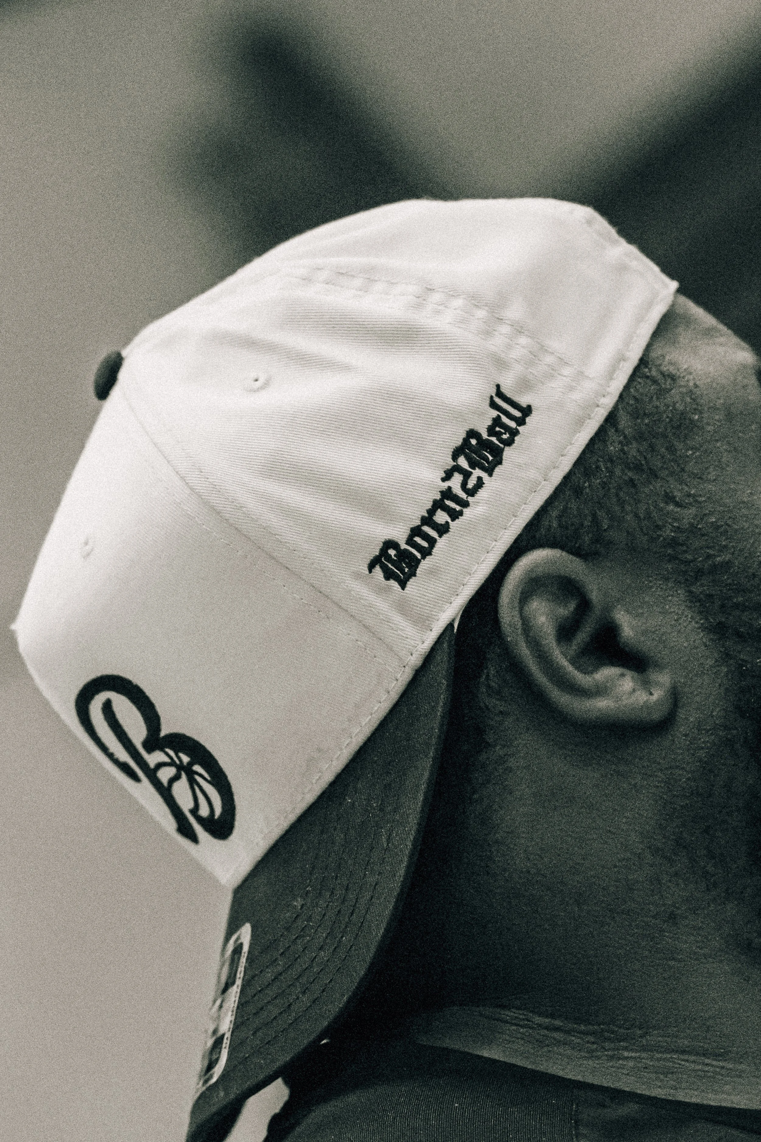 Person wearing a two-tone baseball cap, with front panel and brim in dark color, and side panels in light color, featuring the text 'TRUEMODEL' in black embroidered on the side.