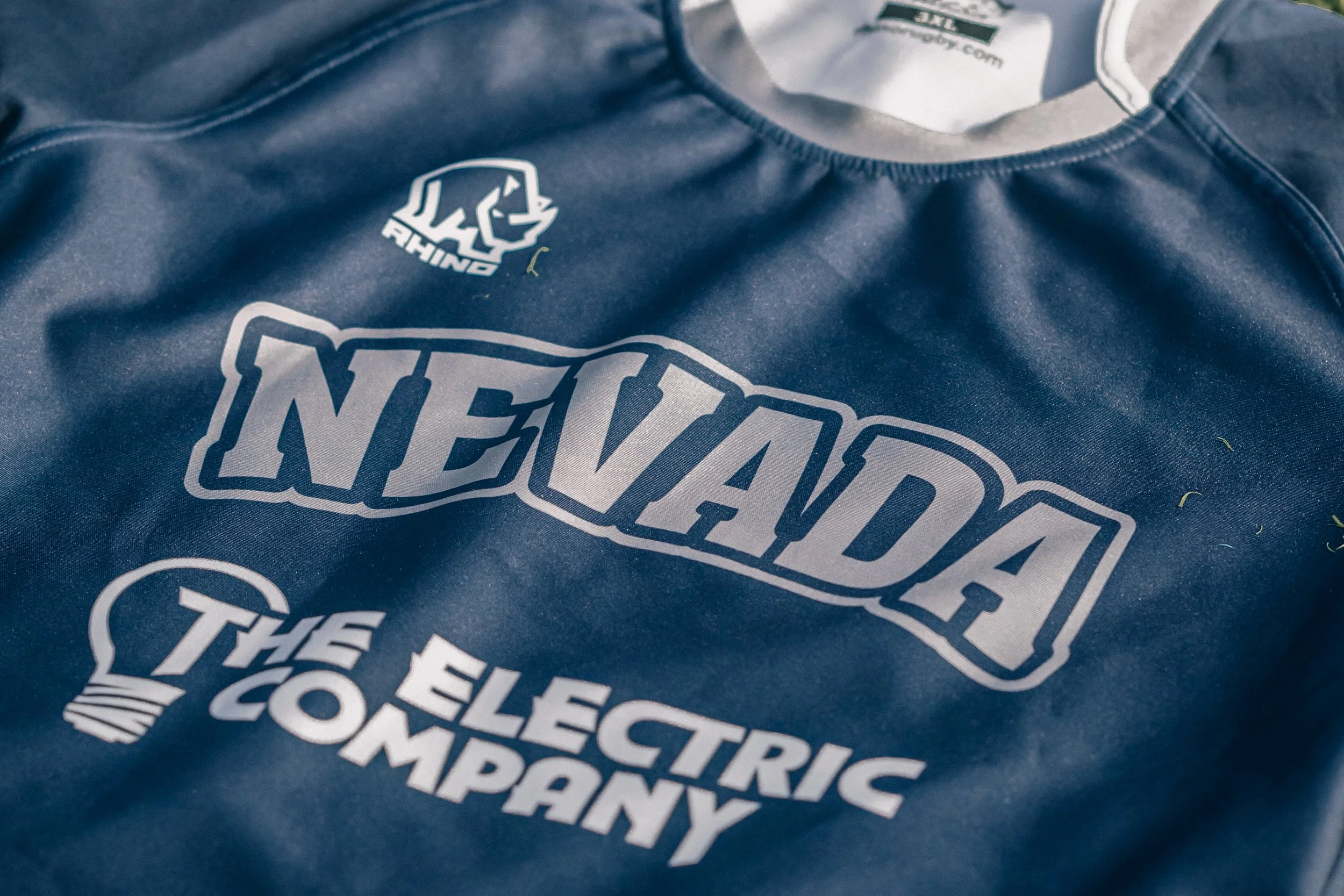 Close-up of a blue sports jersey with the logo of THE NEVADA ELECTRIC COMPANY and a small bear head with the word 'RHINO' above it.
