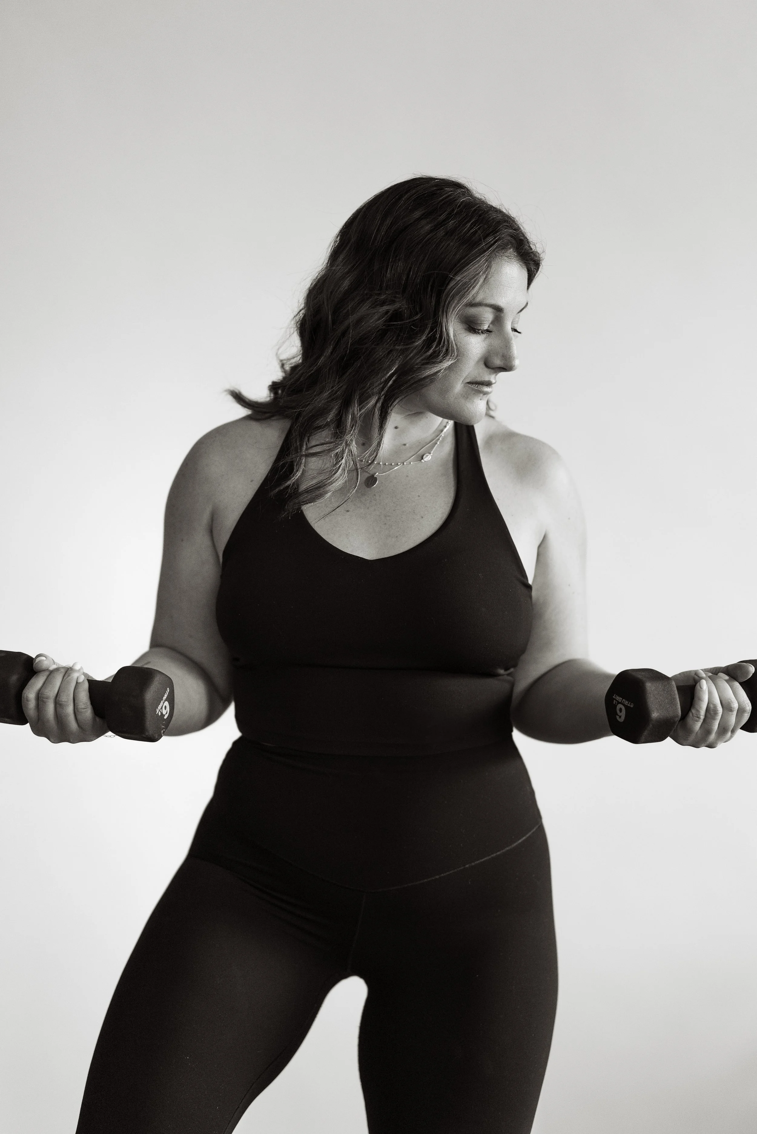 A woman in athletic attire lifting dumbbells in a gym.