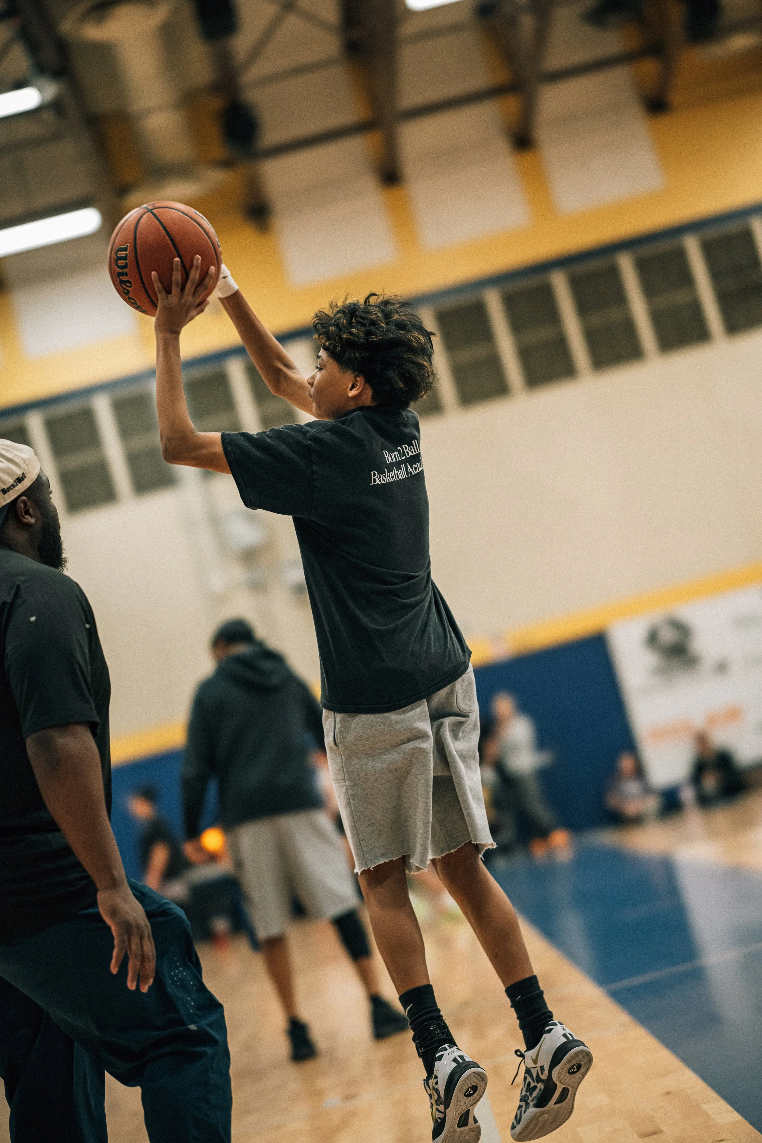 A young man is jumping in a basketball gym, preparing to shoot a basketball.