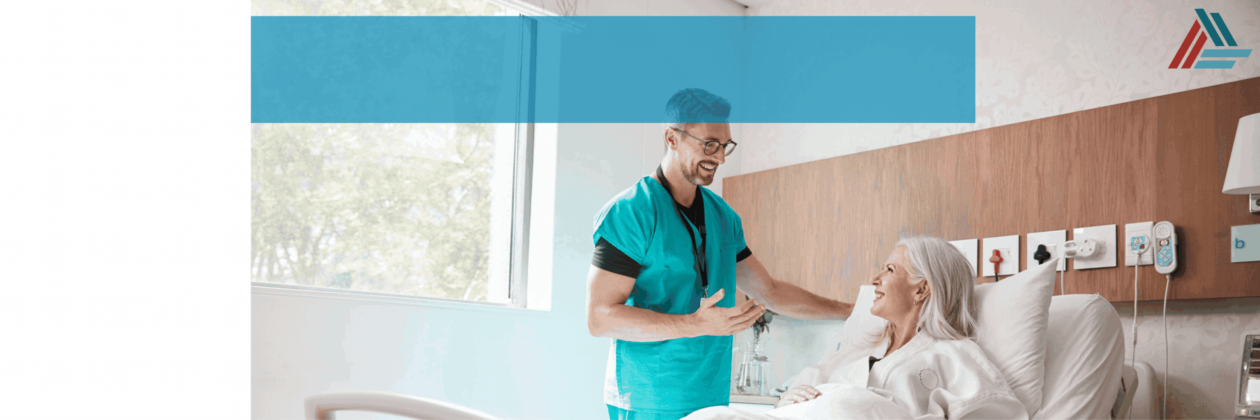 A healthcare worker in teal scrubs smiling and talking to an elderly woman lying in a hospital bed in a bright hospital room.