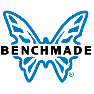 Two men carrying a large piece of meat on a metal frame outdoors on a dirt path, with grassy field and hills in the background during sunset.