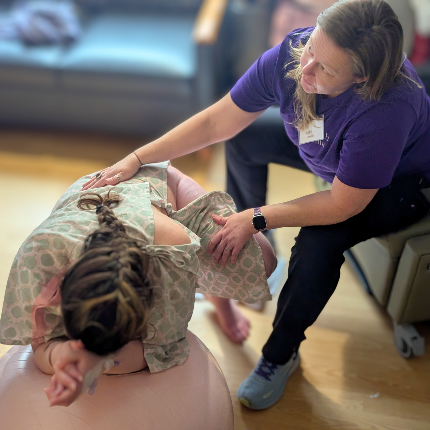 a woman with her hands on the back of another woman who is in labor, laying over an exercise ball