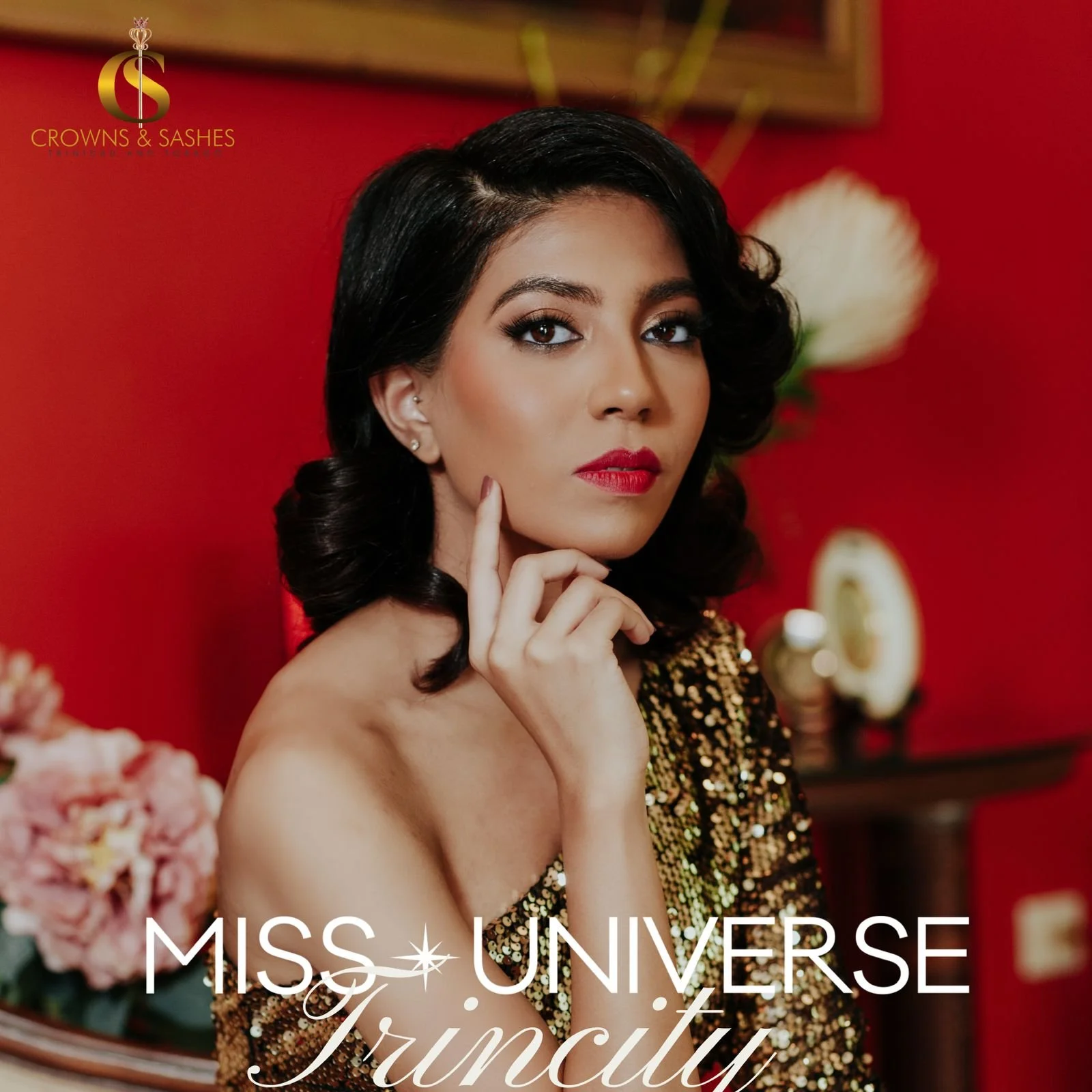 Close-up of a young woman with black hair and red lipstick posing against a red background, wearing a sequined gold dress, with flowers and decorative items in the background.