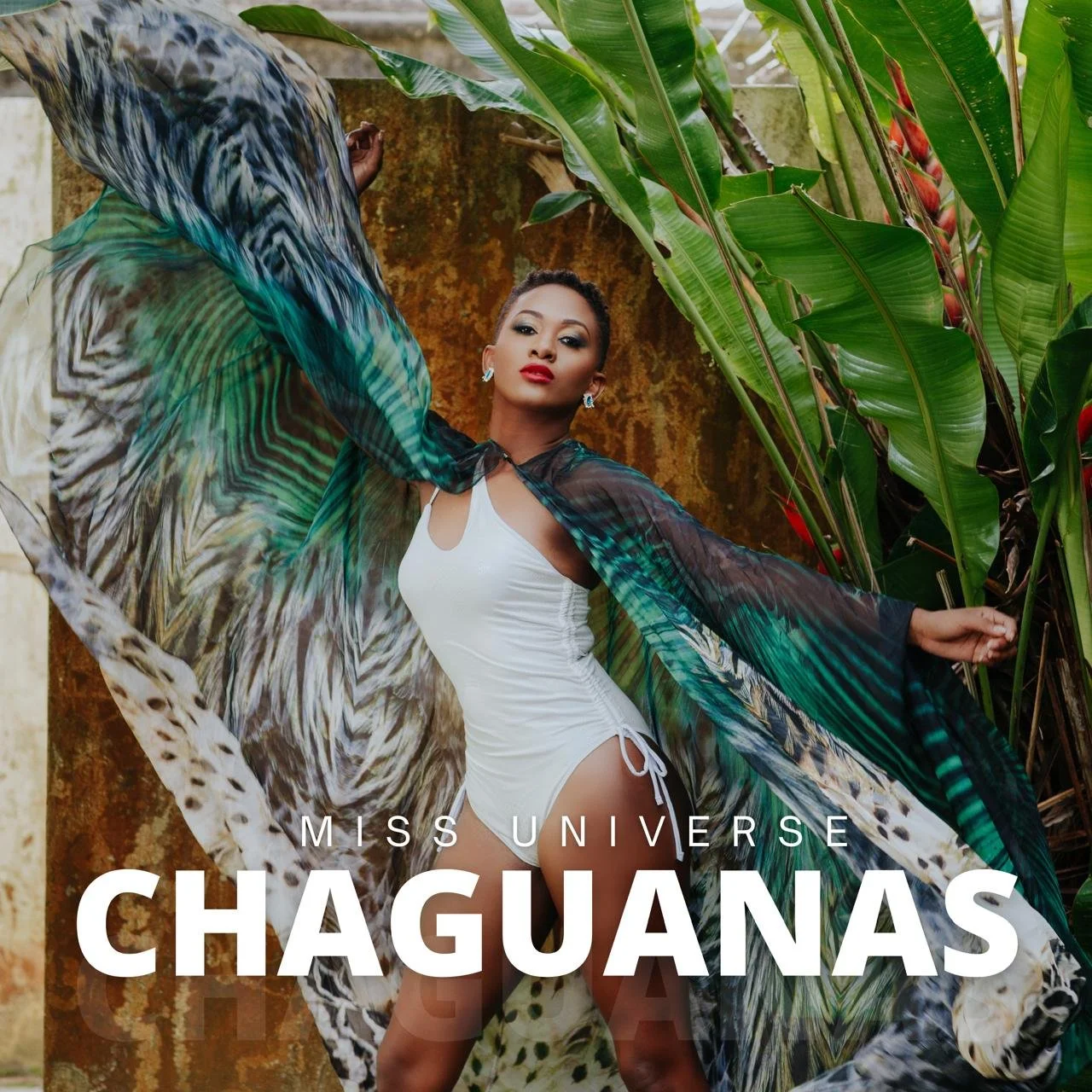 A woman in a white swimsuit with a sheer, tropical patterned cover-up poses among green tropical plants. The photo has text that says 'MISS UNIVERSE CHAGUANAS'.
