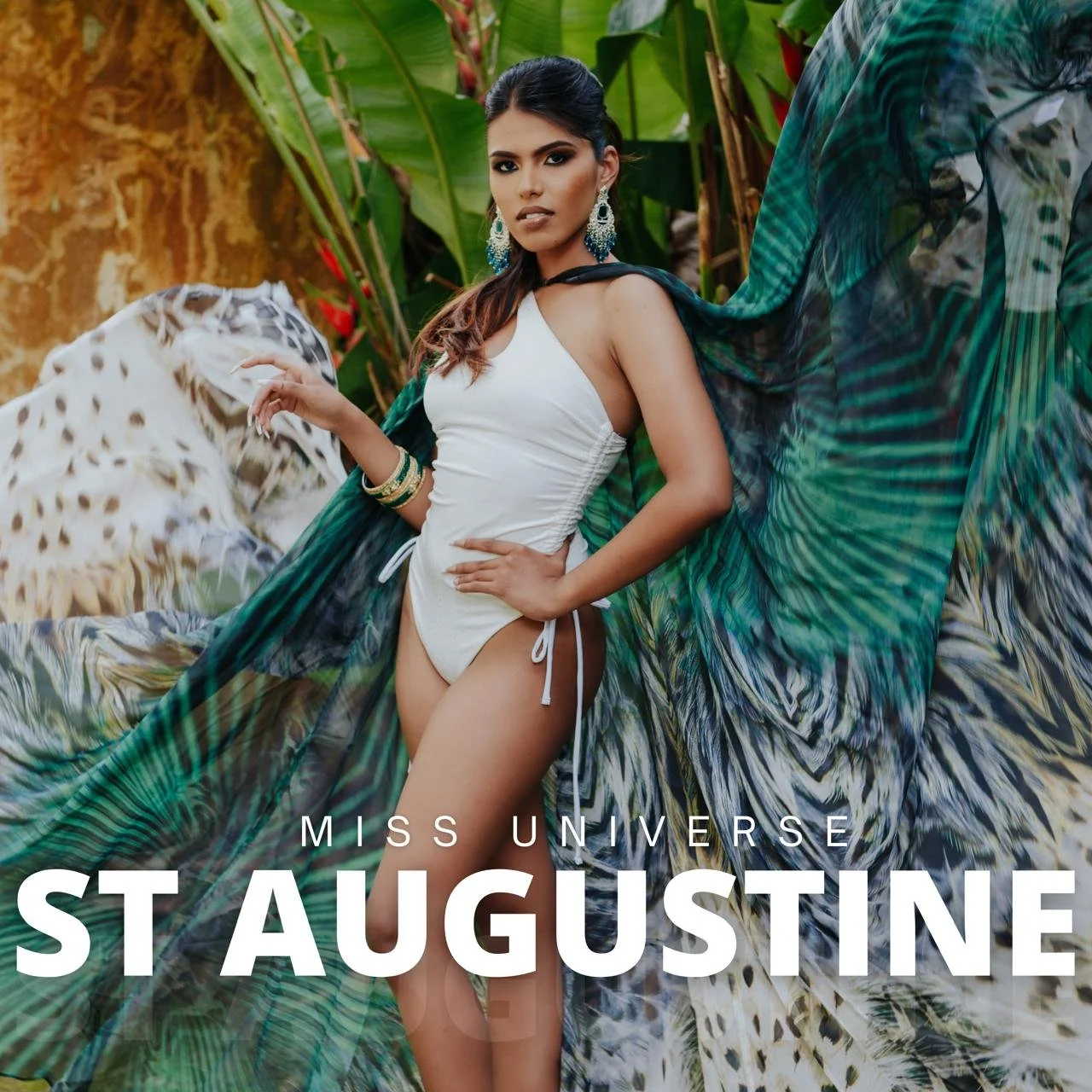 Woman in a white swimsuit with a leopard print cape standing in front of tropical green foliage. She is wearing large earrings and bracelets. The text on the image says 'Miss Universe St. Augustine'.