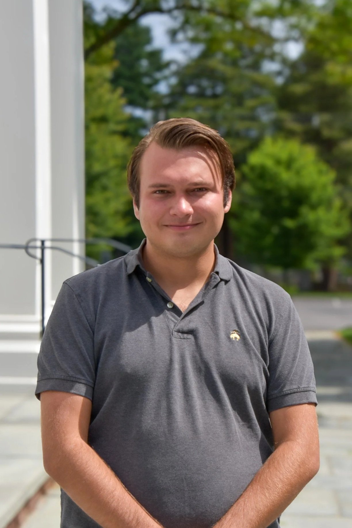 A man woman smiling outdoors with a gray polo shirt on.