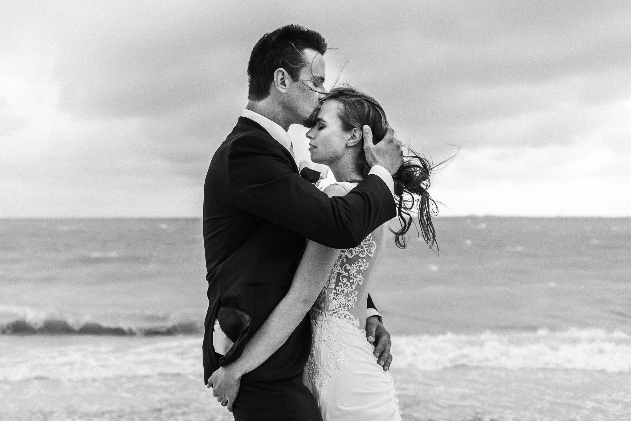 Pareja de novios en la playa, con el fondo del mar y cielo nublado, en un momento romántico, en blanco y negro.
