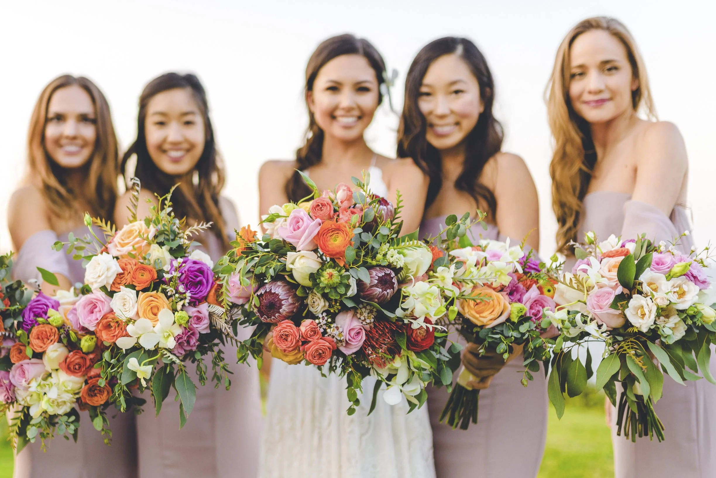 Mujeres con vestido de evento sosteniendo ramos de flores en un jardín.
