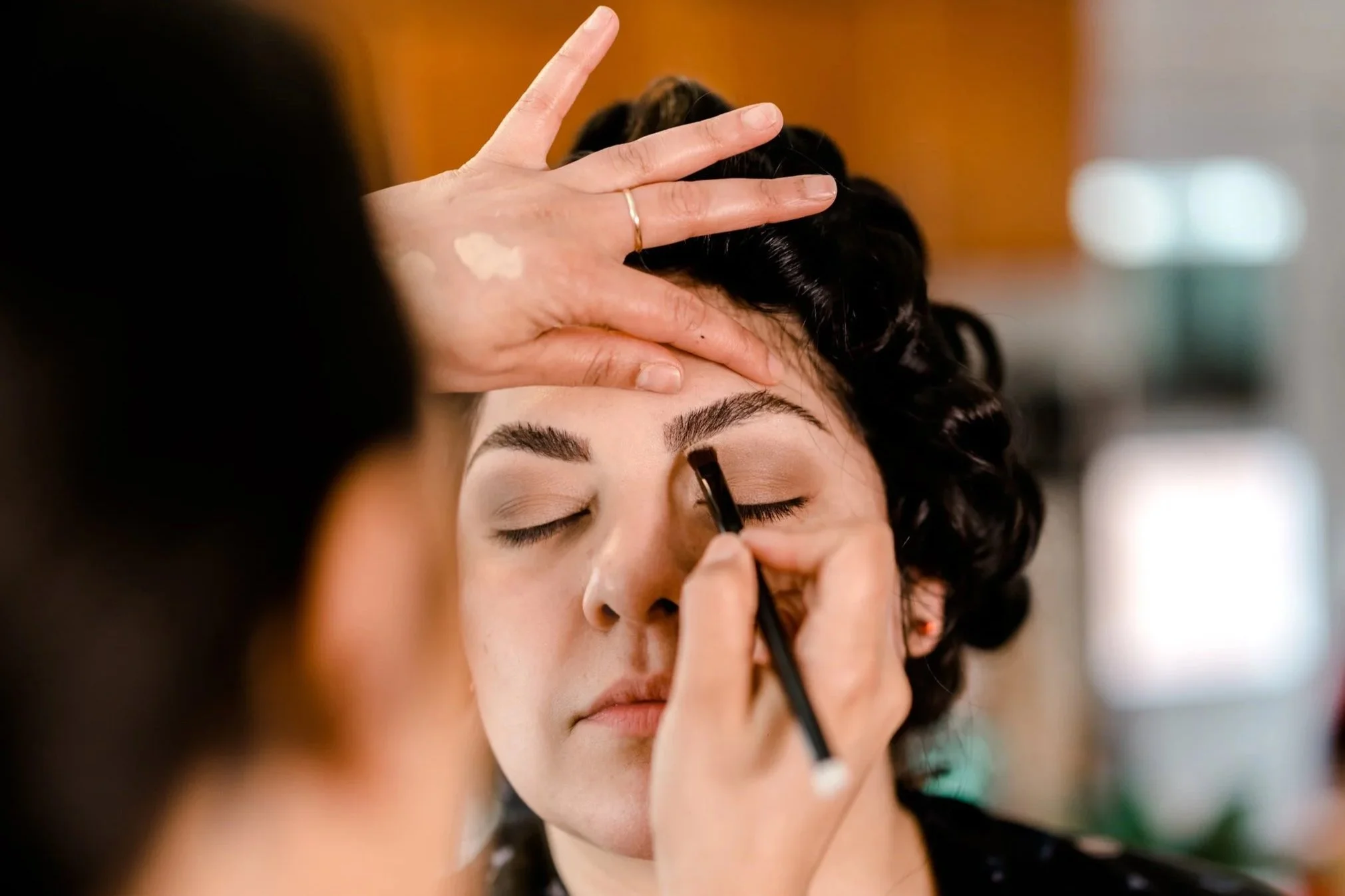 Makeup artist applying eyeliner on a woman's closed eyelid.